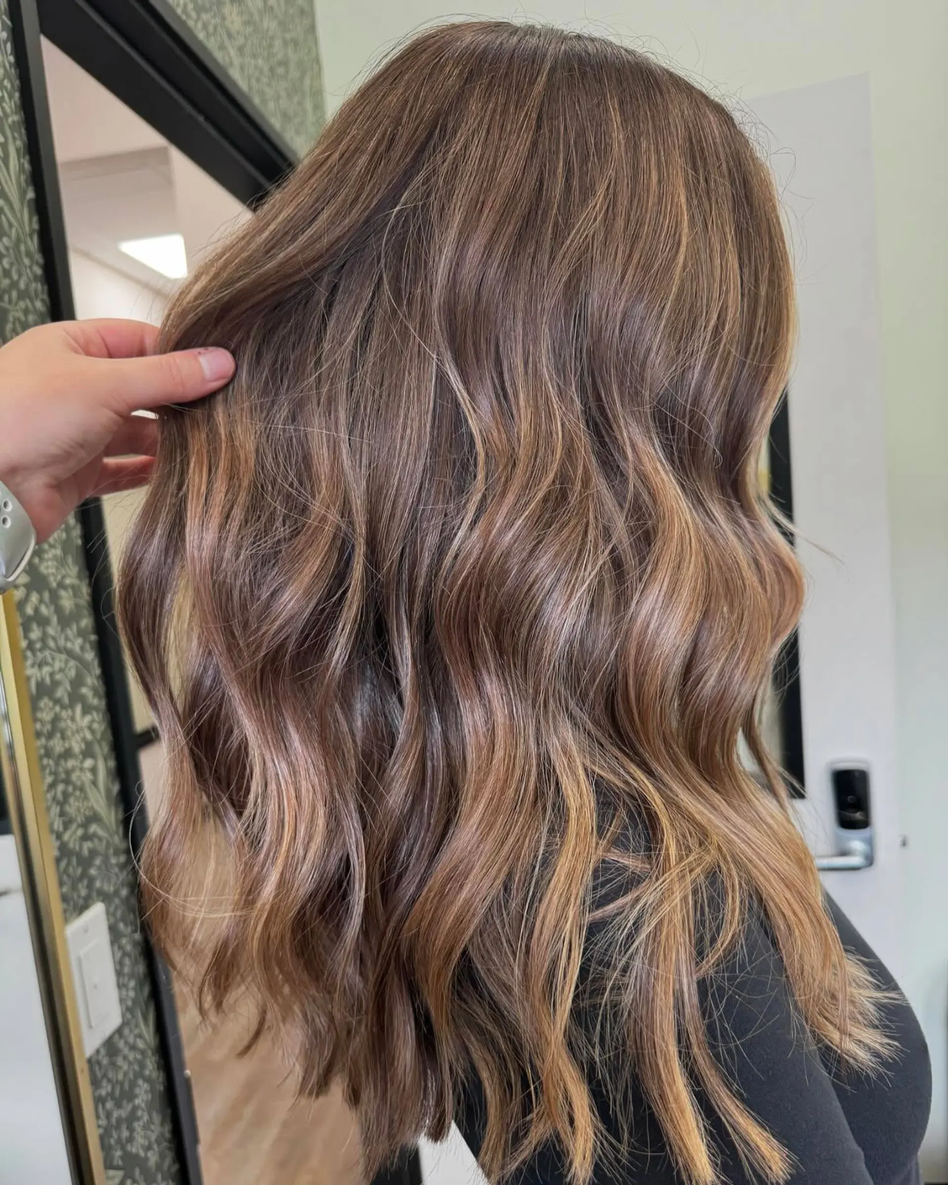 Long hair styled in soft textured waves featuring a natural bronde balayage with caramel and golden blonde highlights. 1