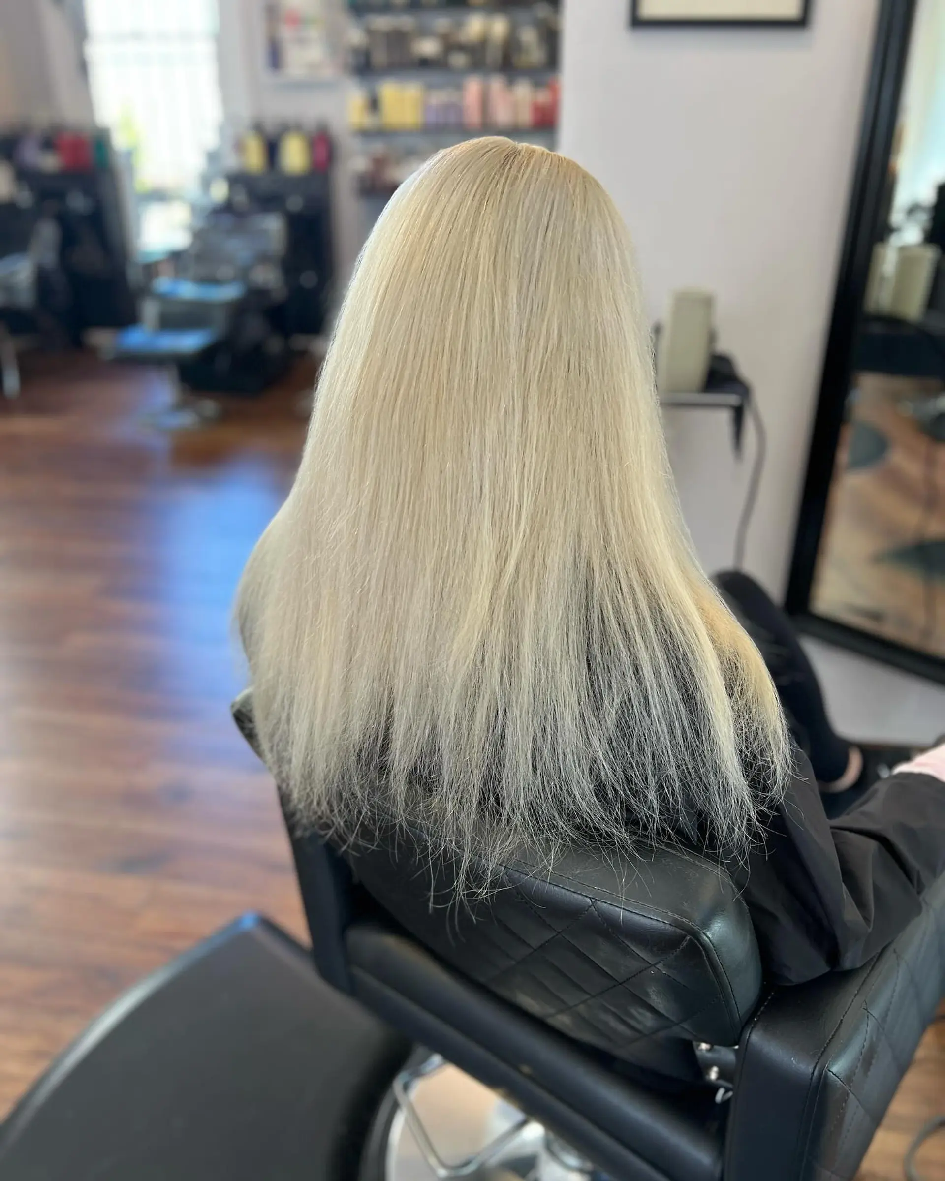 Long, straight icy platinum blonde hair extensions shown from behind in a salon setting. 1