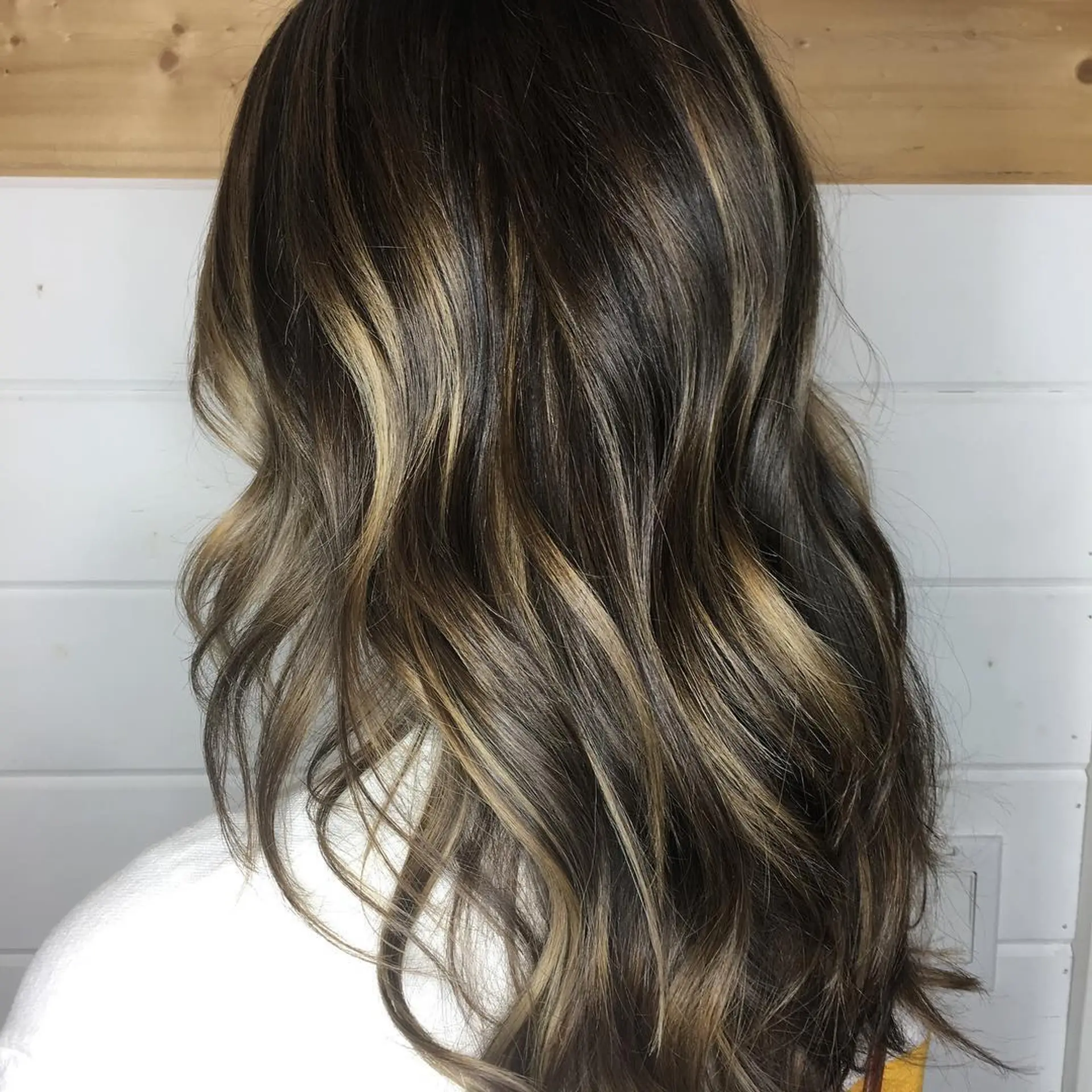 Long brunette hair styled in loose waves with dimensional caramel balayage highlights. 1