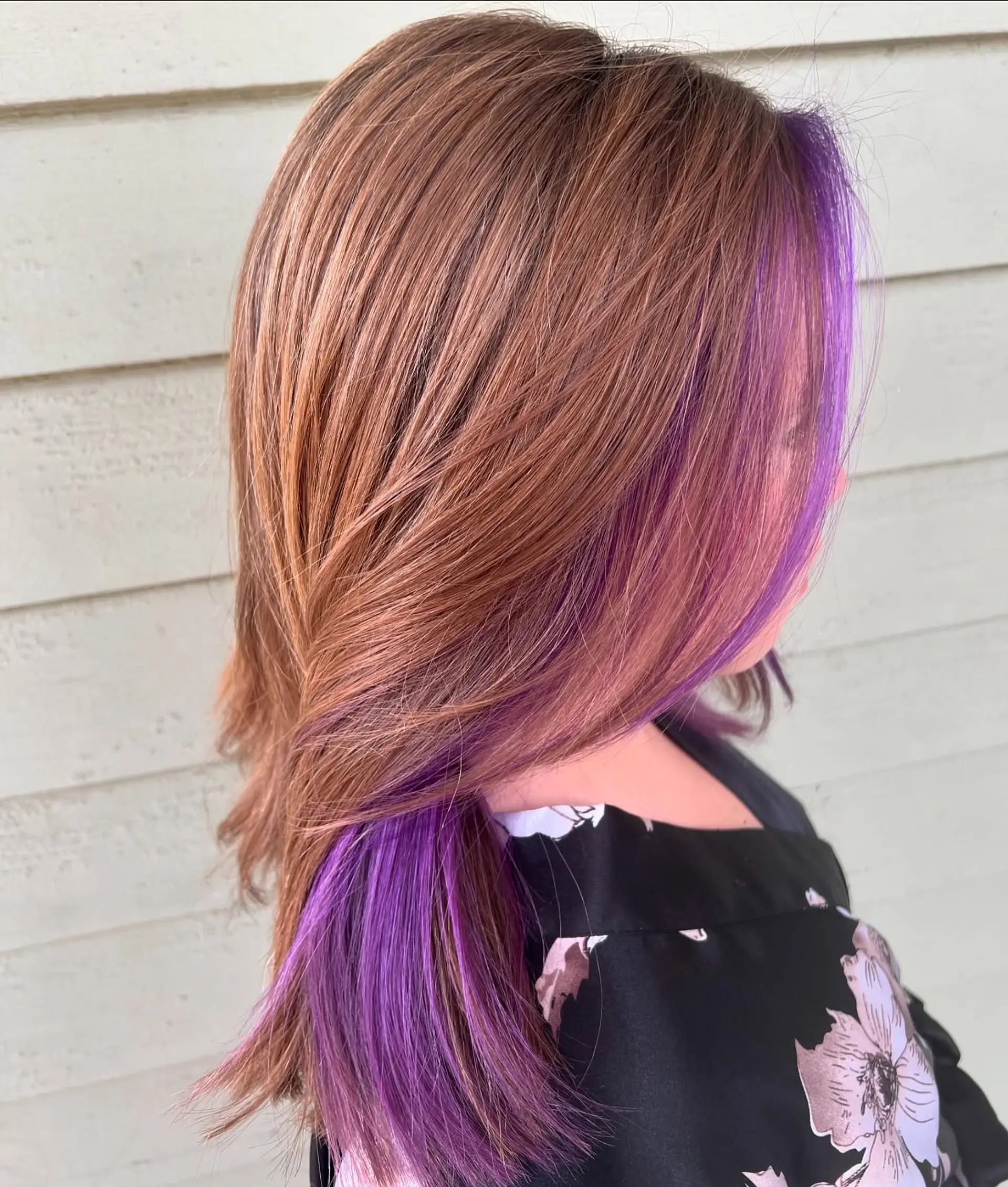 A medium-length, layered cut featuring soft waves. The hair is colored with a dimensional rose gold and warm brown base, highlighted by striking purple peek-a-boo sections underneath. 2