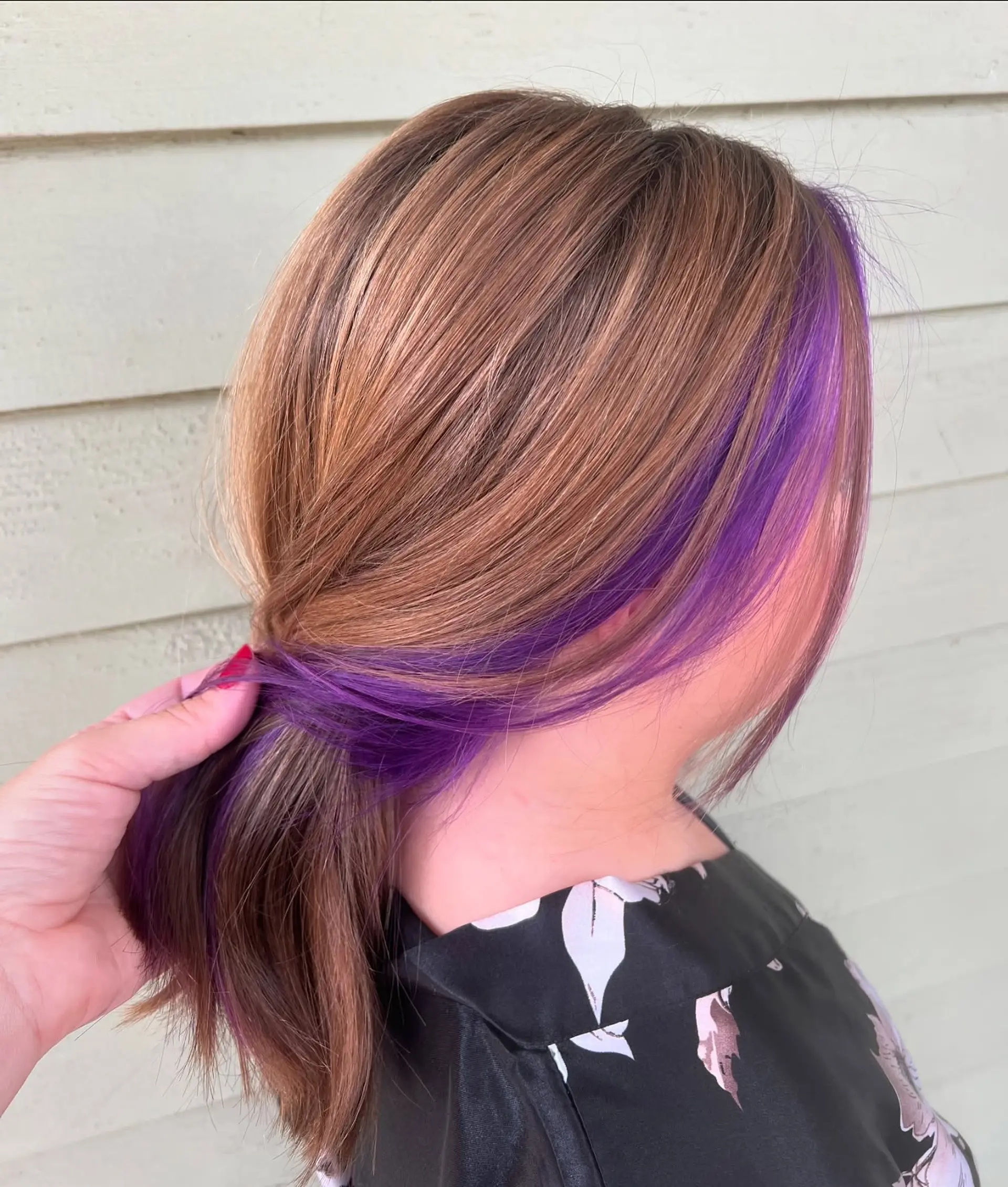 A medium-length, layered cut featuring soft waves. The hair is colored with a dimensional rose gold and warm brown base, highlighted by striking purple peek-a-boo sections underneath. 3