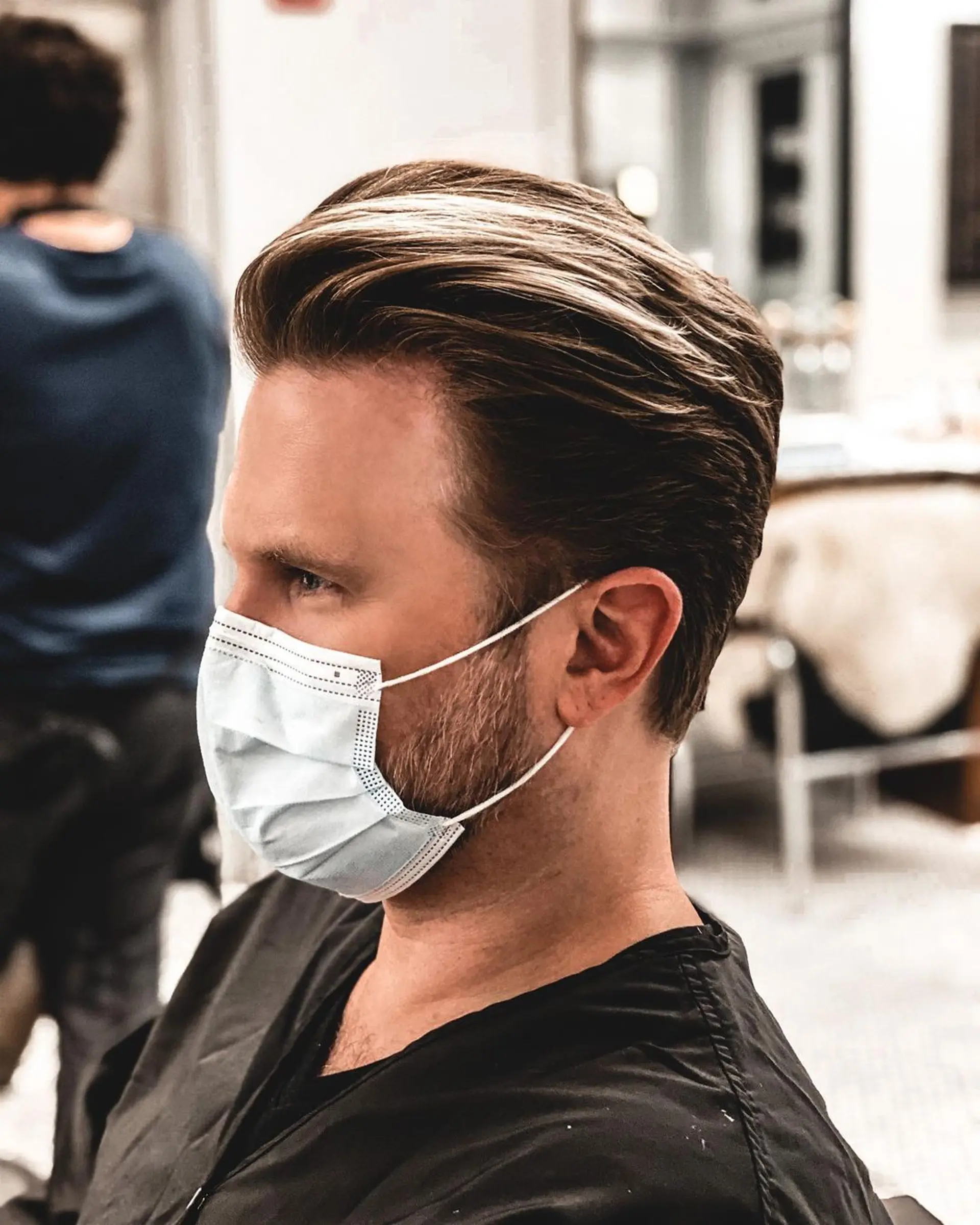 A sophisticated hairstyle with medium-length, straight light brown hair and subtle blond highlights. The style features volume at the crown, smoothly brushed back hair, and neatly faded sides, complemented by a well-groomed beard. 1