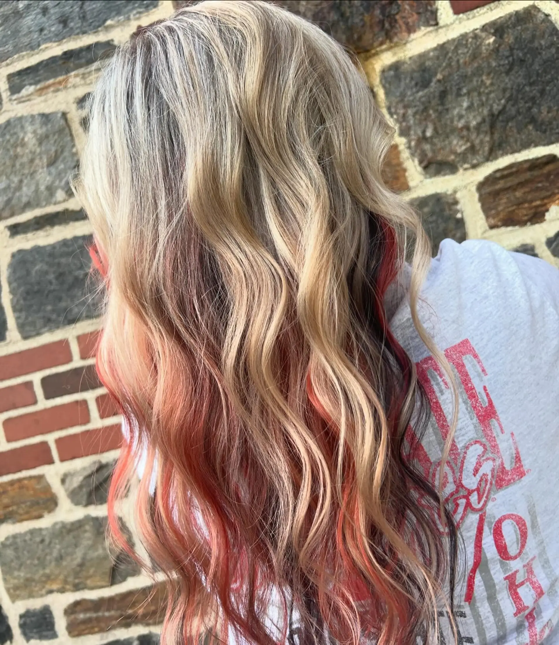 Long wavy blonde hair showcasing a vibrant red and dark peekaboo color underlayer. 1