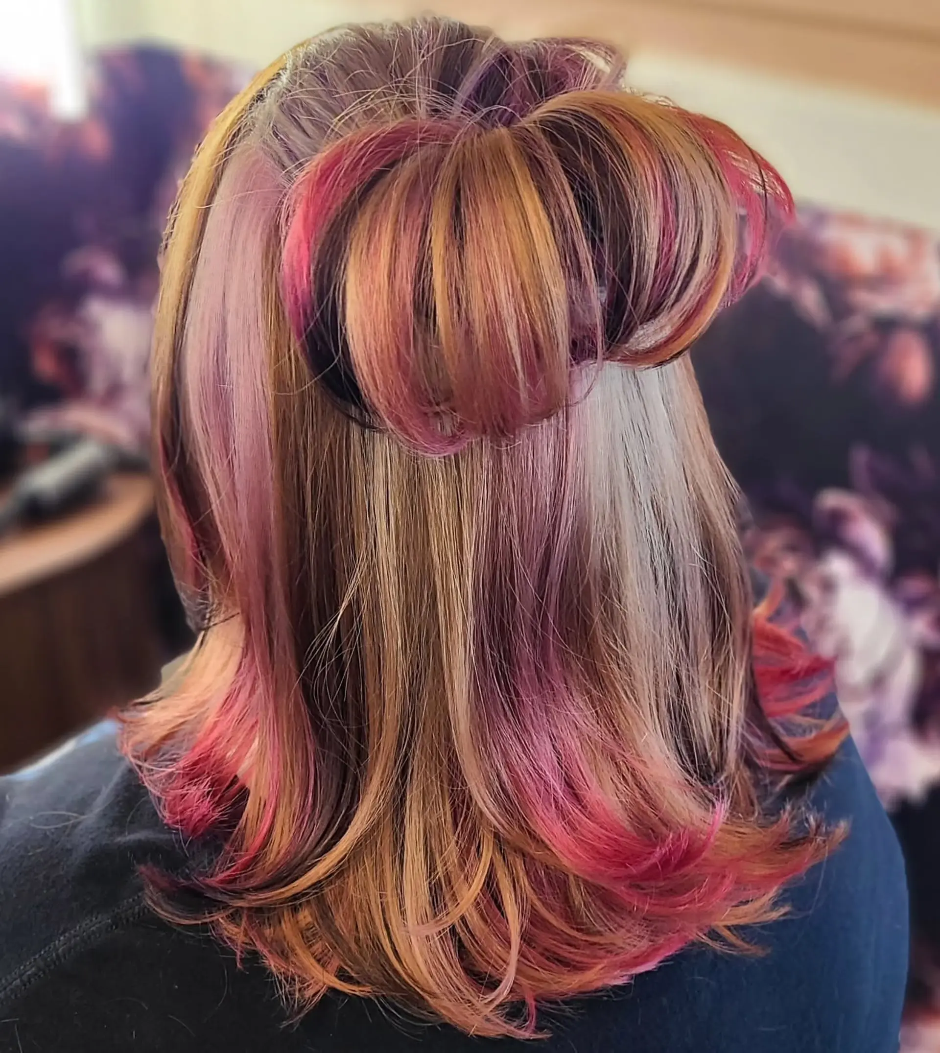 A medium-length, straight hairstyle showcasing a dynamic multi-tonal color palette. It features a blend of natural base colors with bold vivid pink, magenta, and lavender highlights, styled with a chic half-up messy bun. 1