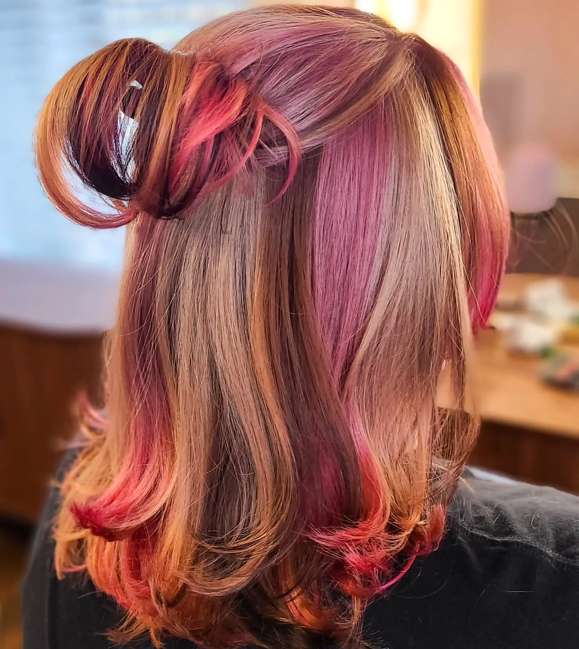 A medium-length, straight hairstyle showcasing a dynamic multi-tonal color palette. It features a blend of natural base colors with bold vivid pink, magenta, and lavender highlights, styled with a chic half-up messy bun. 2