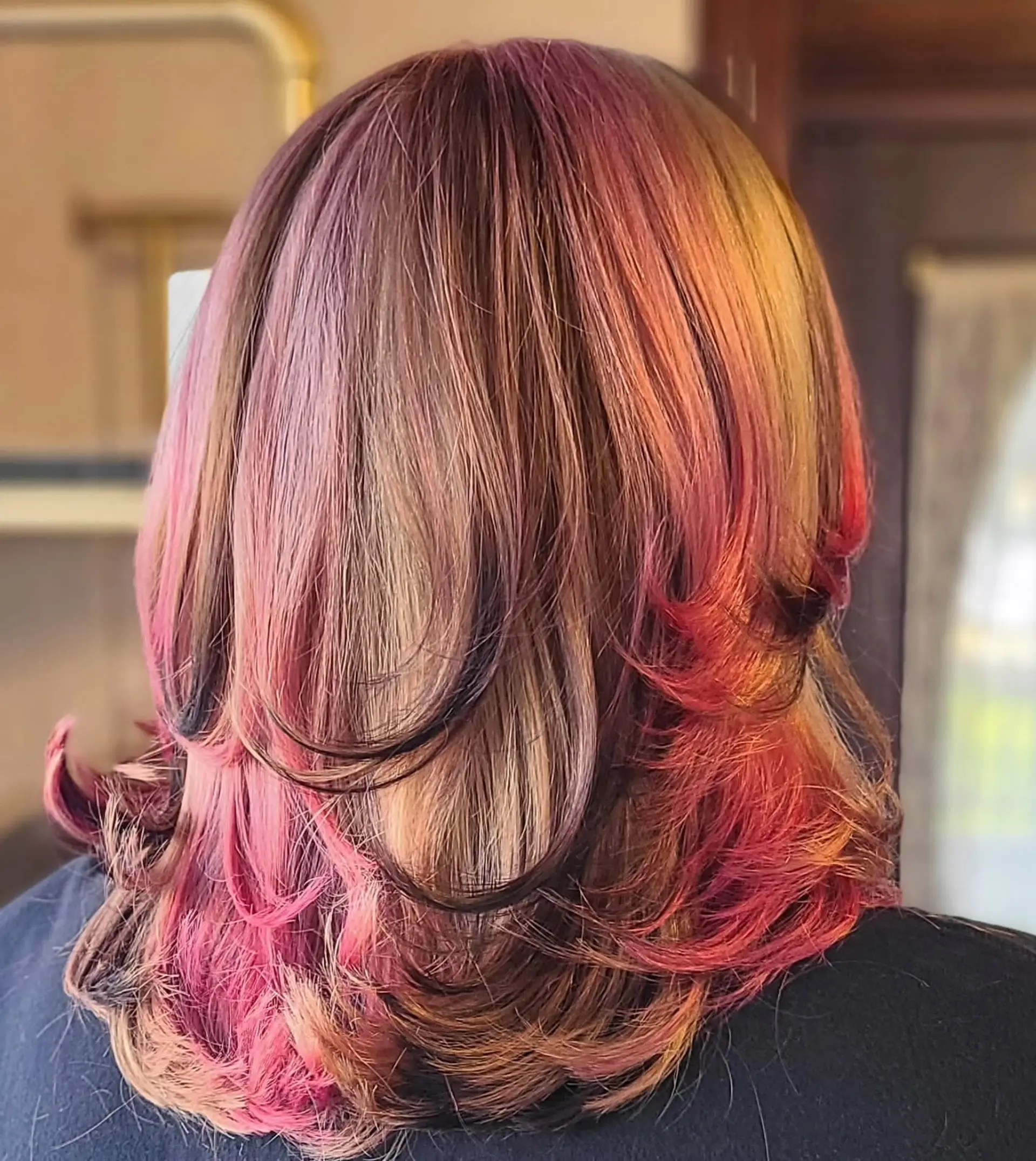 A medium-length, straight hairstyle showcasing a dynamic multi-tonal color palette. It features a blend of natural base colors with bold vivid pink, magenta, and lavender highlights, styled with a chic half-up messy bun. 3