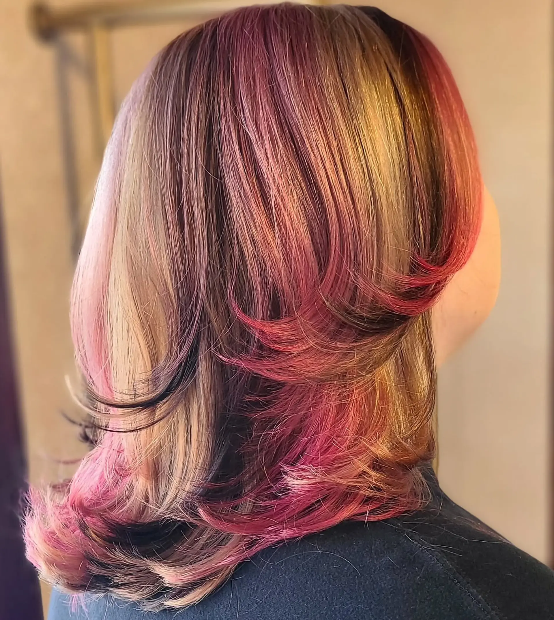 A medium-length, straight hairstyle showcasing a dynamic multi-tonal color palette. It features a blend of natural base colors with bold vivid pink, magenta, and lavender highlights, styled with a chic half-up messy bun. 4