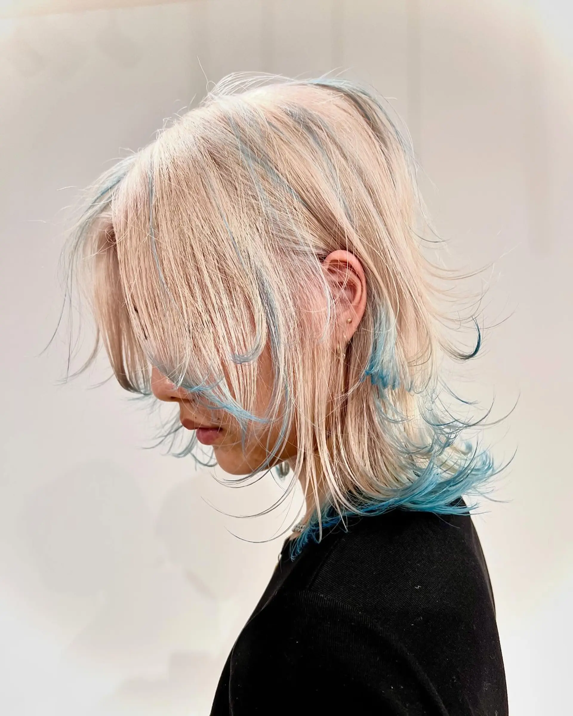 Layered, medium-length, straight hair in platinum blonde with teal highlights, featuring a soft fringe and feathered ends. 1