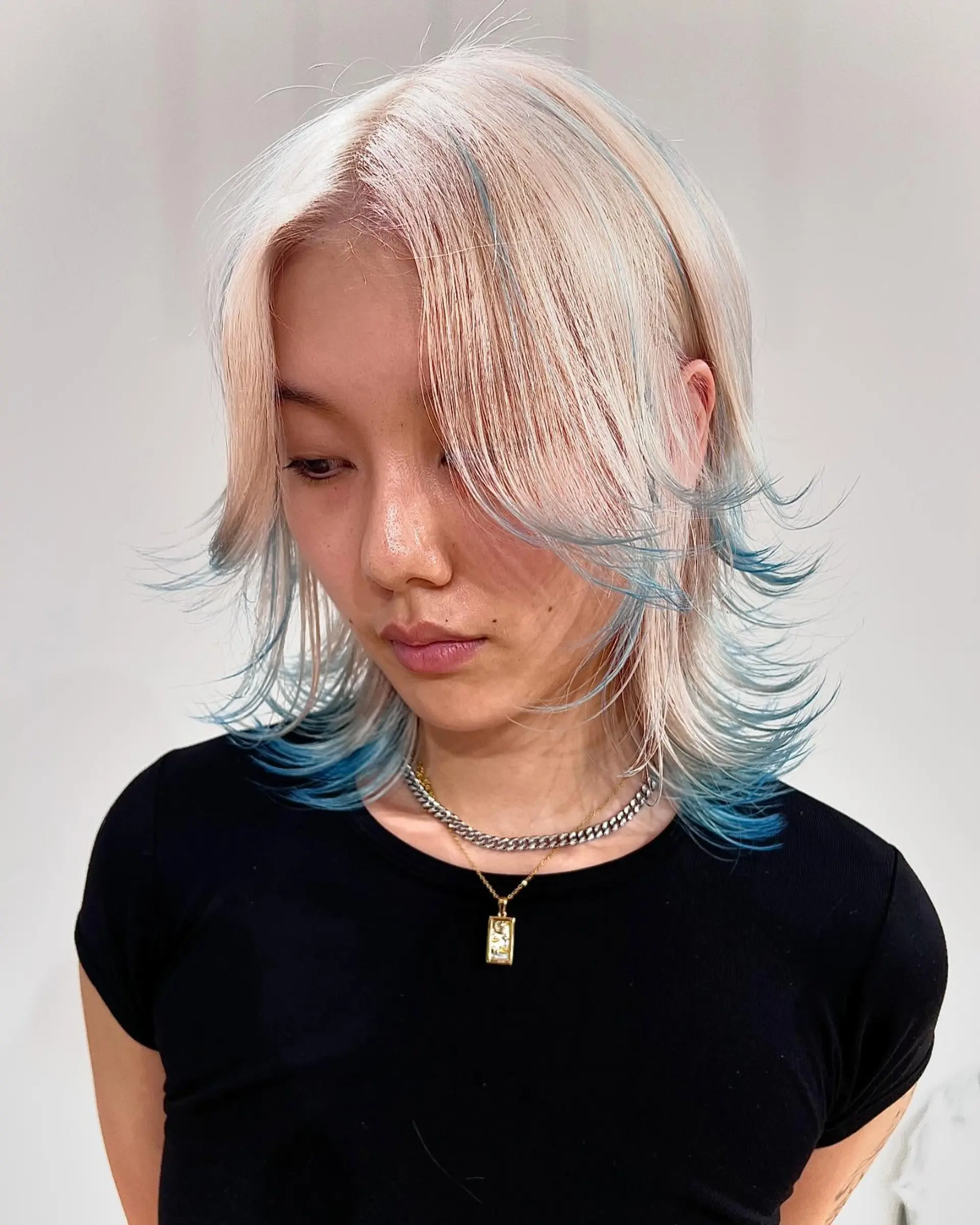 Layered, medium-length, straight hair in platinum blonde with teal highlights, featuring a soft fringe and feathered ends. 2