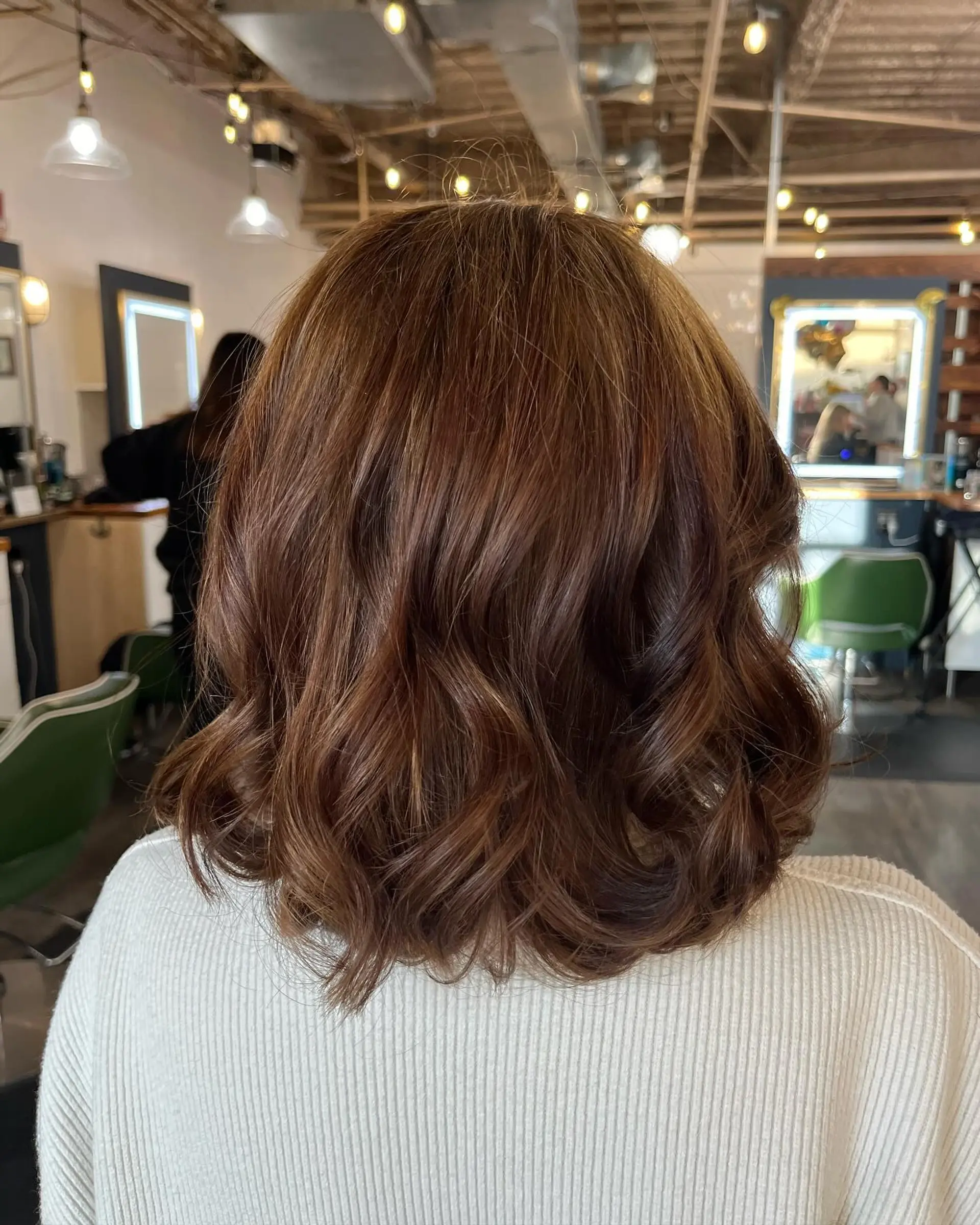 Shoulder-length dimensional warm brunette hair styled with loose, polished waves and curled ends. 1