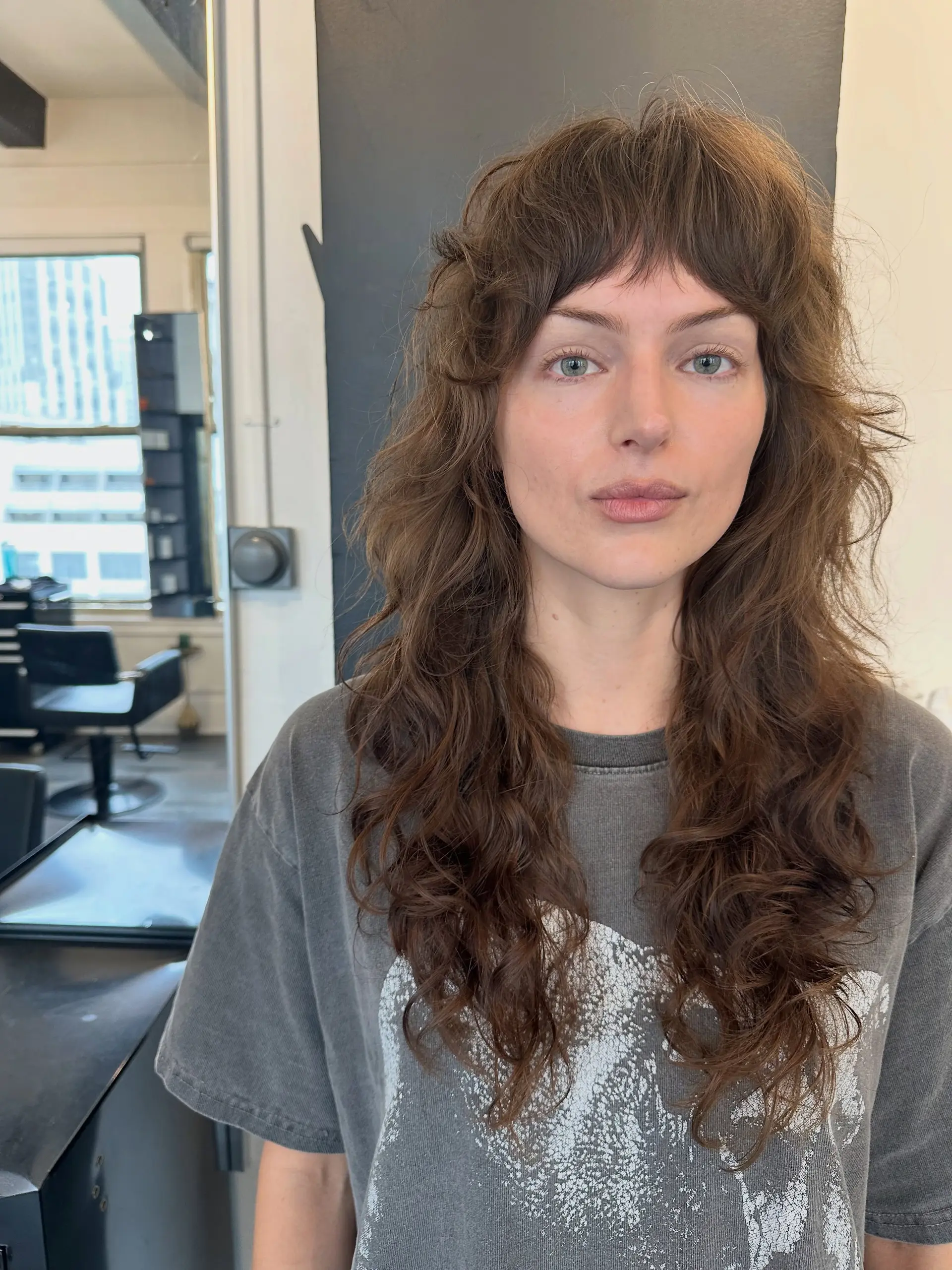 A textured long shag haircut featuring face-framing layers, choppy bangs, and effortless wavy texture. 1