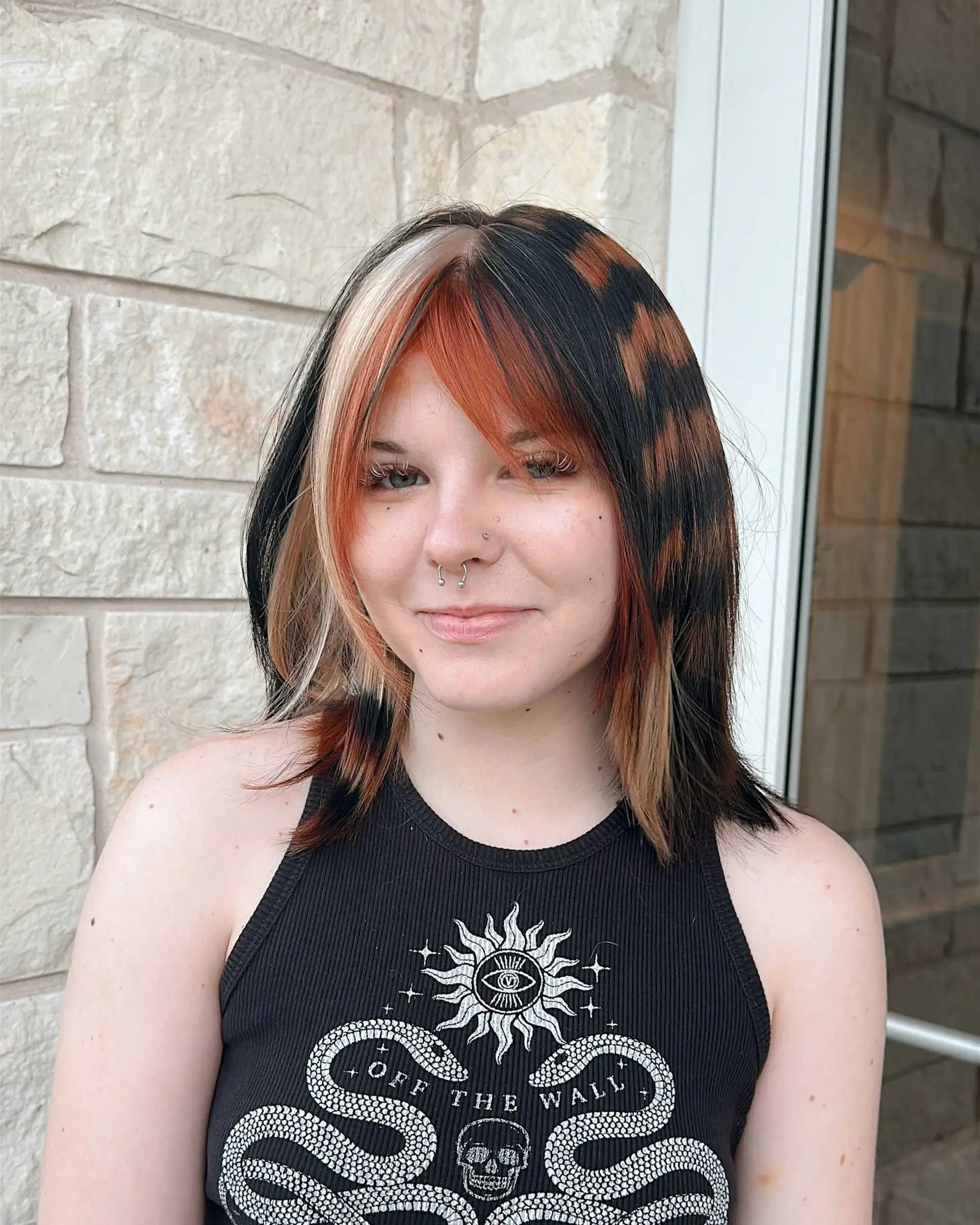 This medium-length layered cut features dramatic fringe bangs and bold, contrasting color panels. The style includes vivid copper, chunky blonde highlights, and an intricate leopard print pattern on a darker hair base, creating a distinct alternative aesthetic. 1