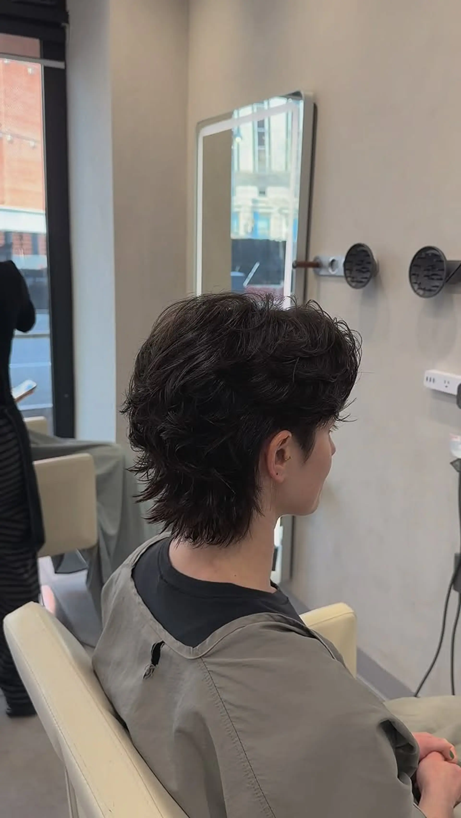 A short, textured wolf cut featuring soft permed waves, feathered layers around the crown, and a tapered nape. 1