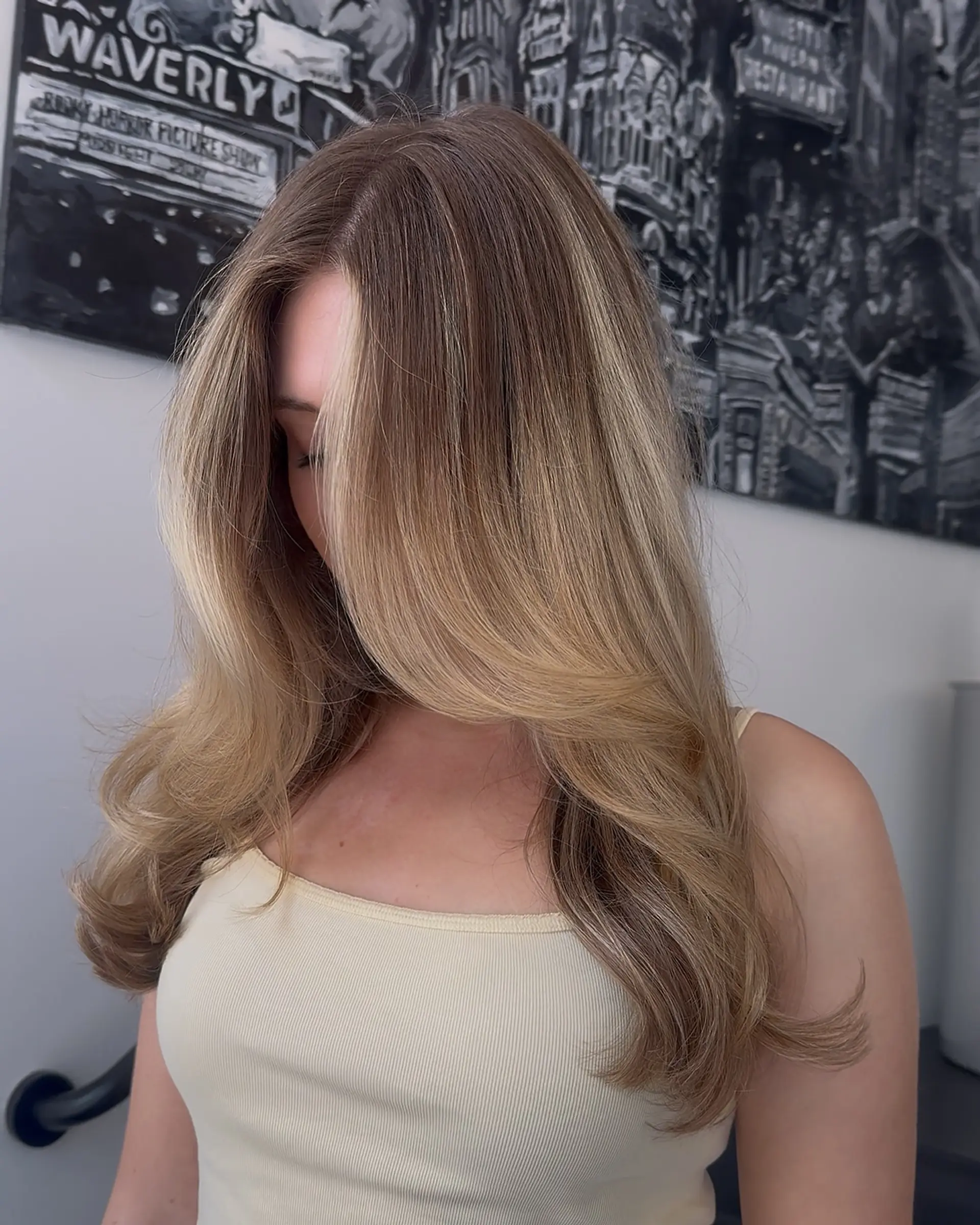 Long warm blonde hair cut with subtle, face-framing layers and styled into a voluminous blowout with soft curved ends. 1