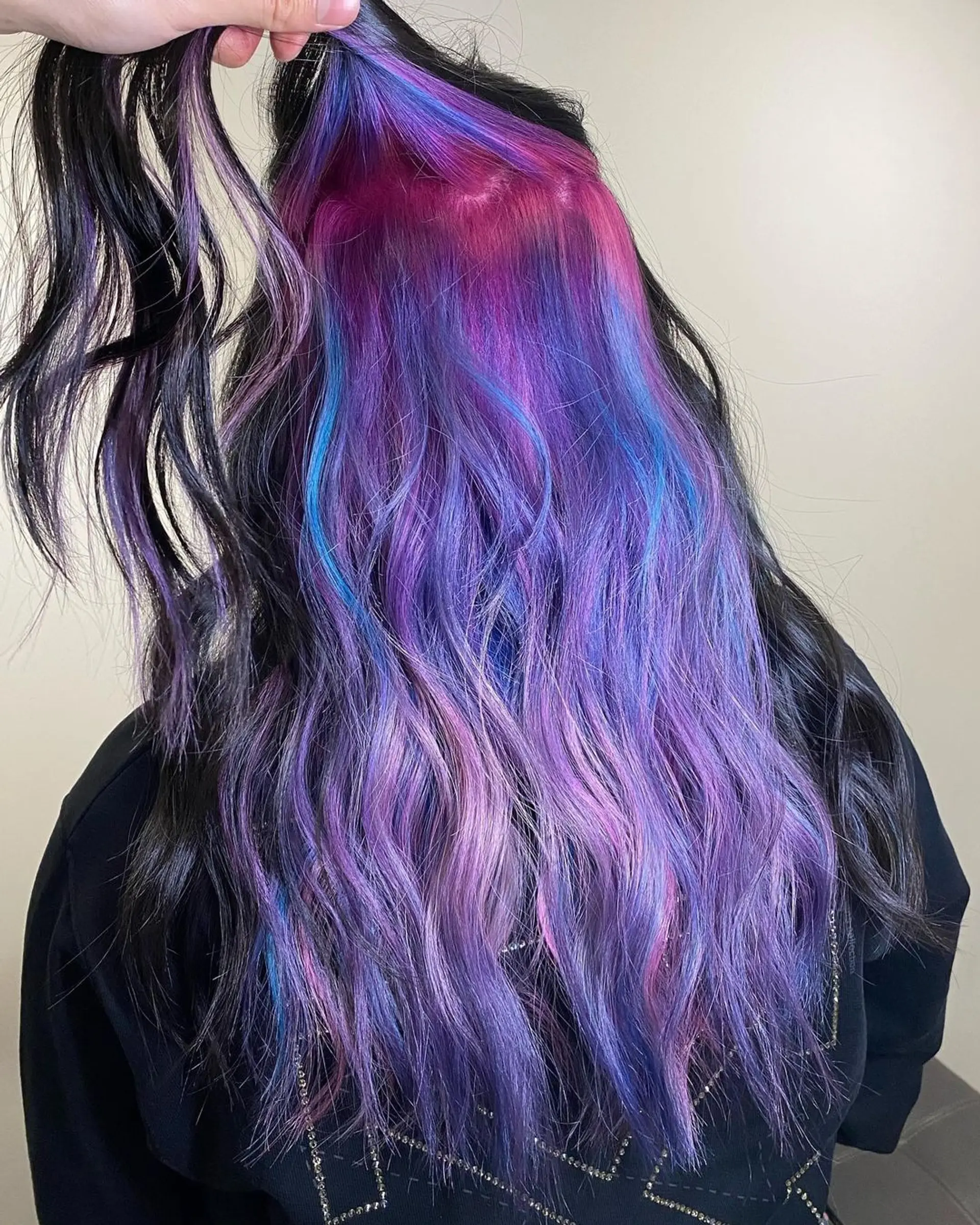 Captivating long wavy hairstyle featuring an ombre effect transitioning from deep black roots to hues of purple, lavender, and indigo with soft, natural waves and subtle layering to enhance volume and movement. 1