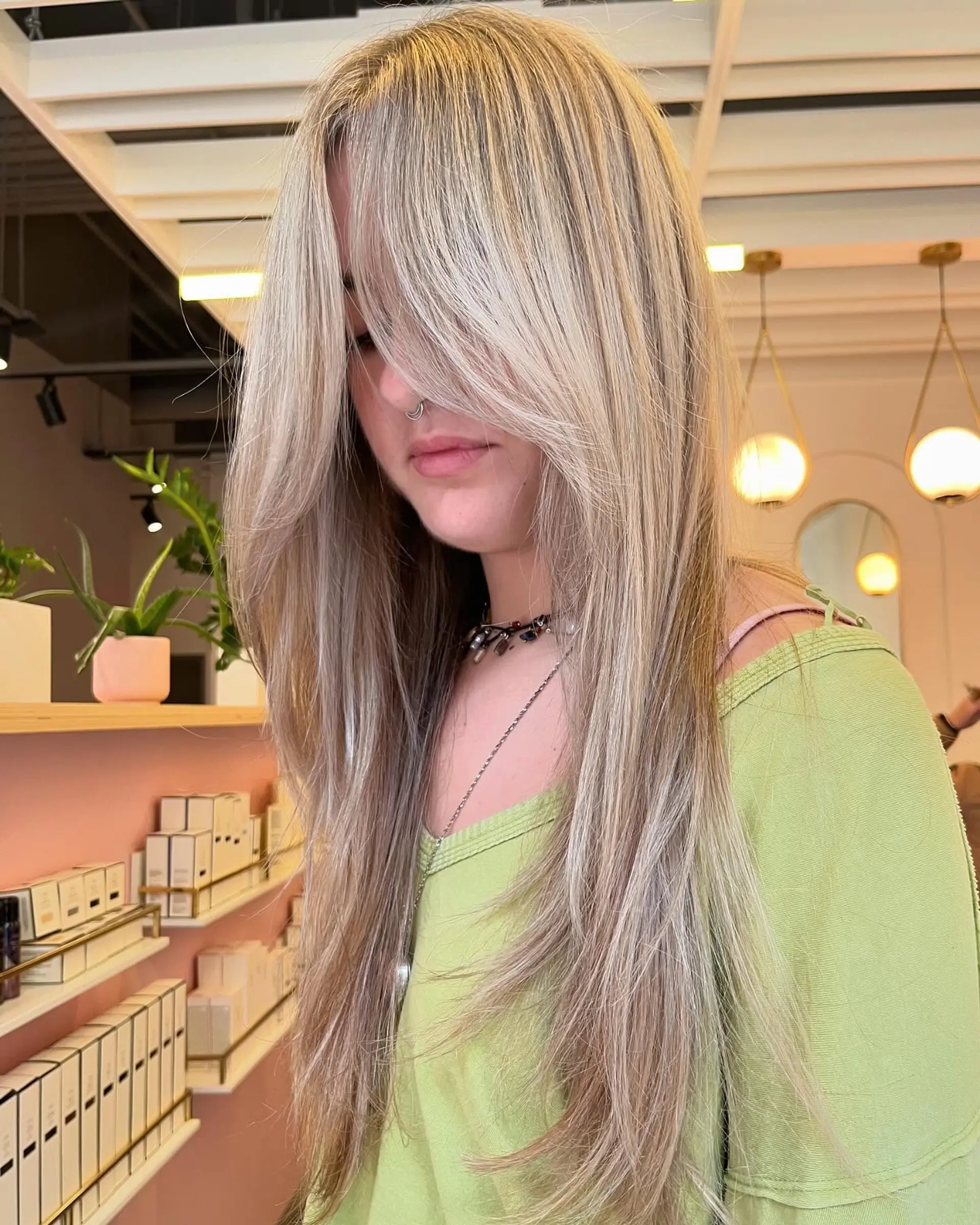 Long beige-blonde hair cut with heavy face-framing curtain bangs and soft, textured layers styled straight with curved ends. 1