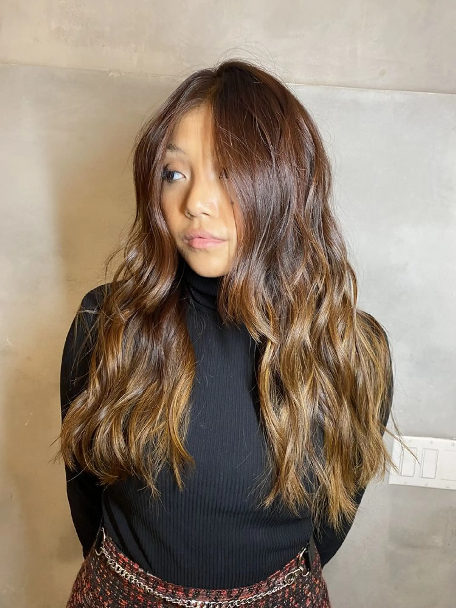 A long, wavy hairstyle with a rich brown base and honey blonde highlights, featuring a natural, voluminous look enhanced by a side part. 1