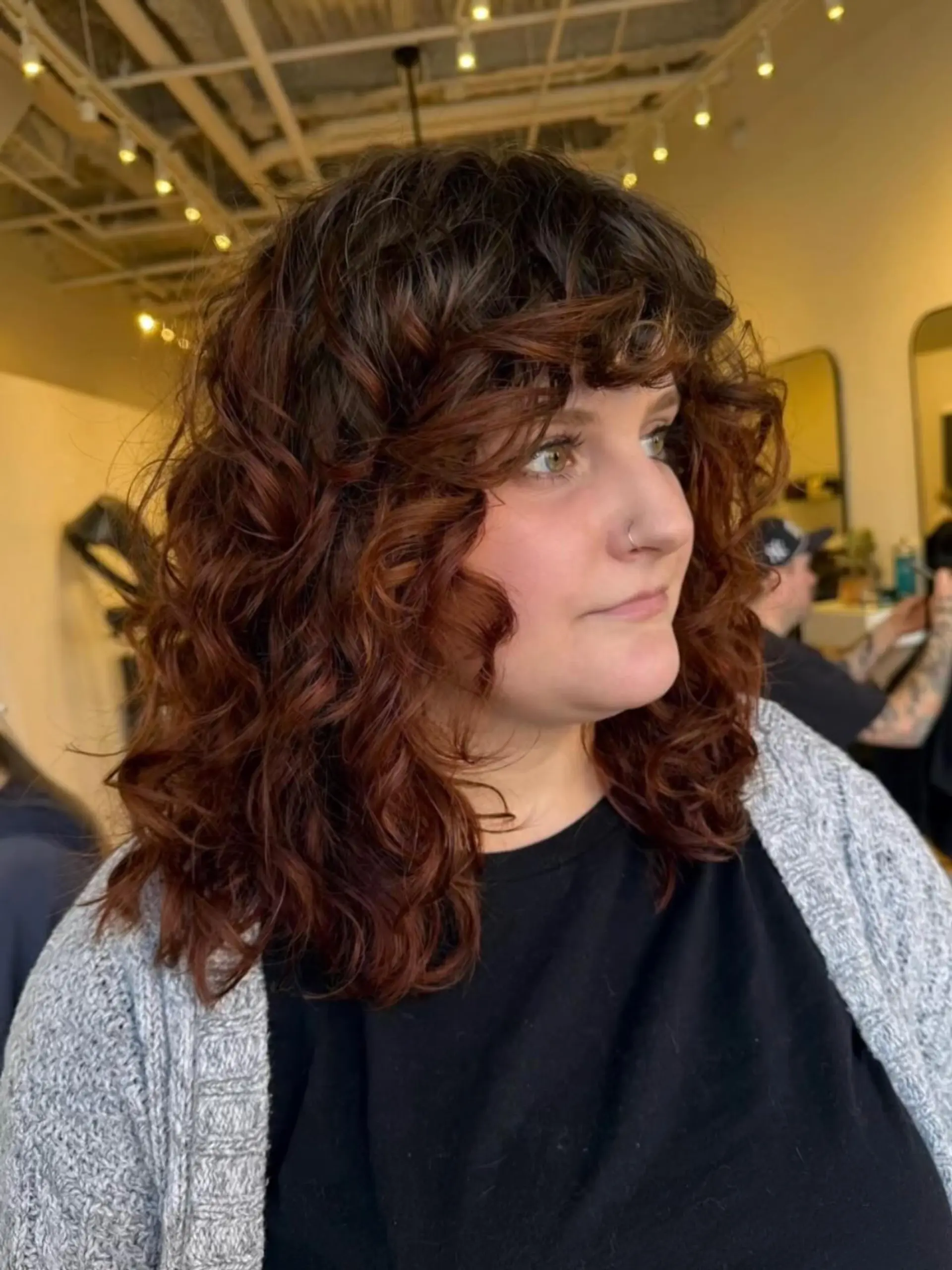 Medium-length curly shag featuring face-framing curly bangs and warm auburn-toned highlights. 1