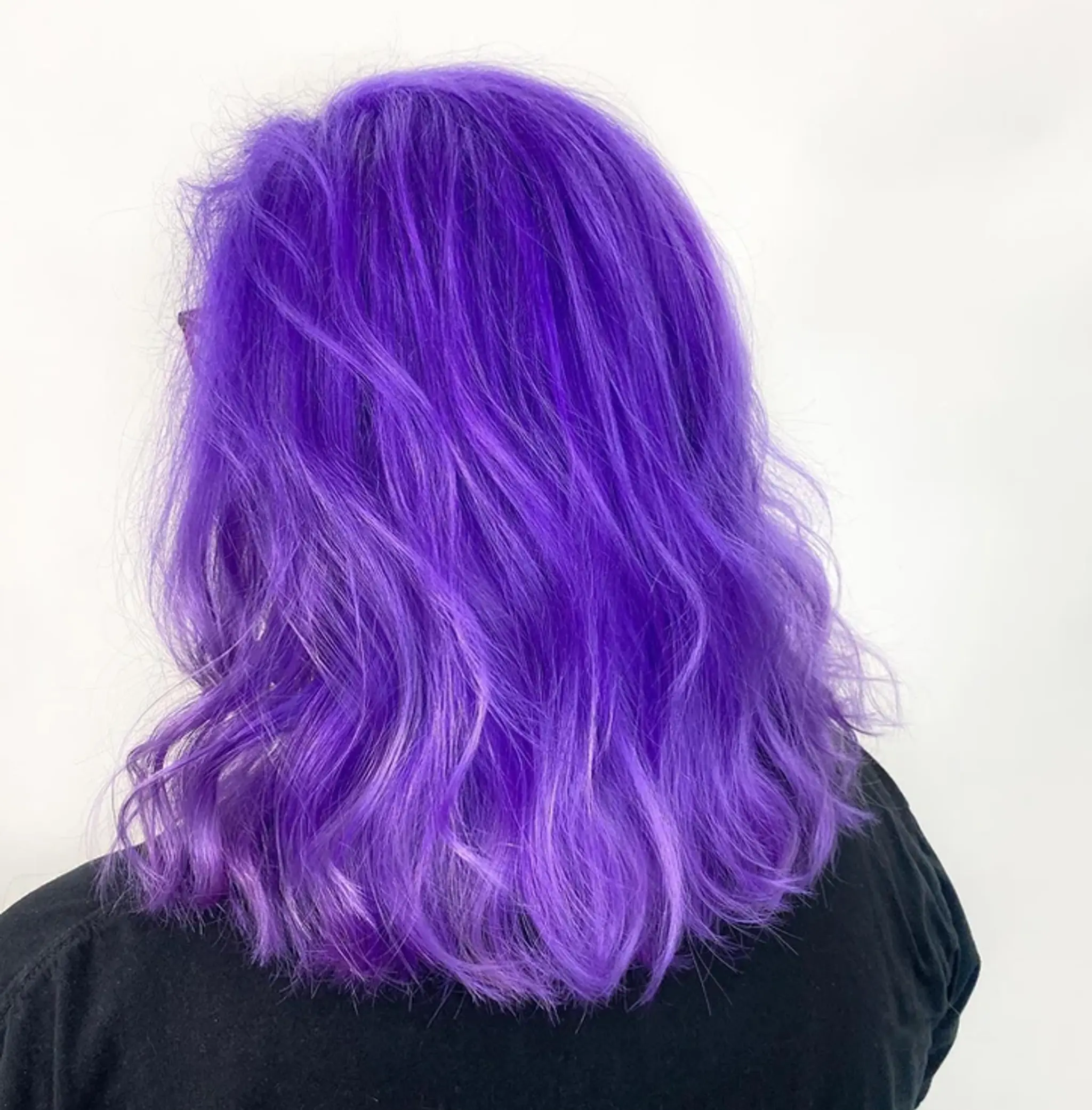 Medium-length, wavy hair in vibrant purple with lavender undertones, creating a voluminous and chic look.