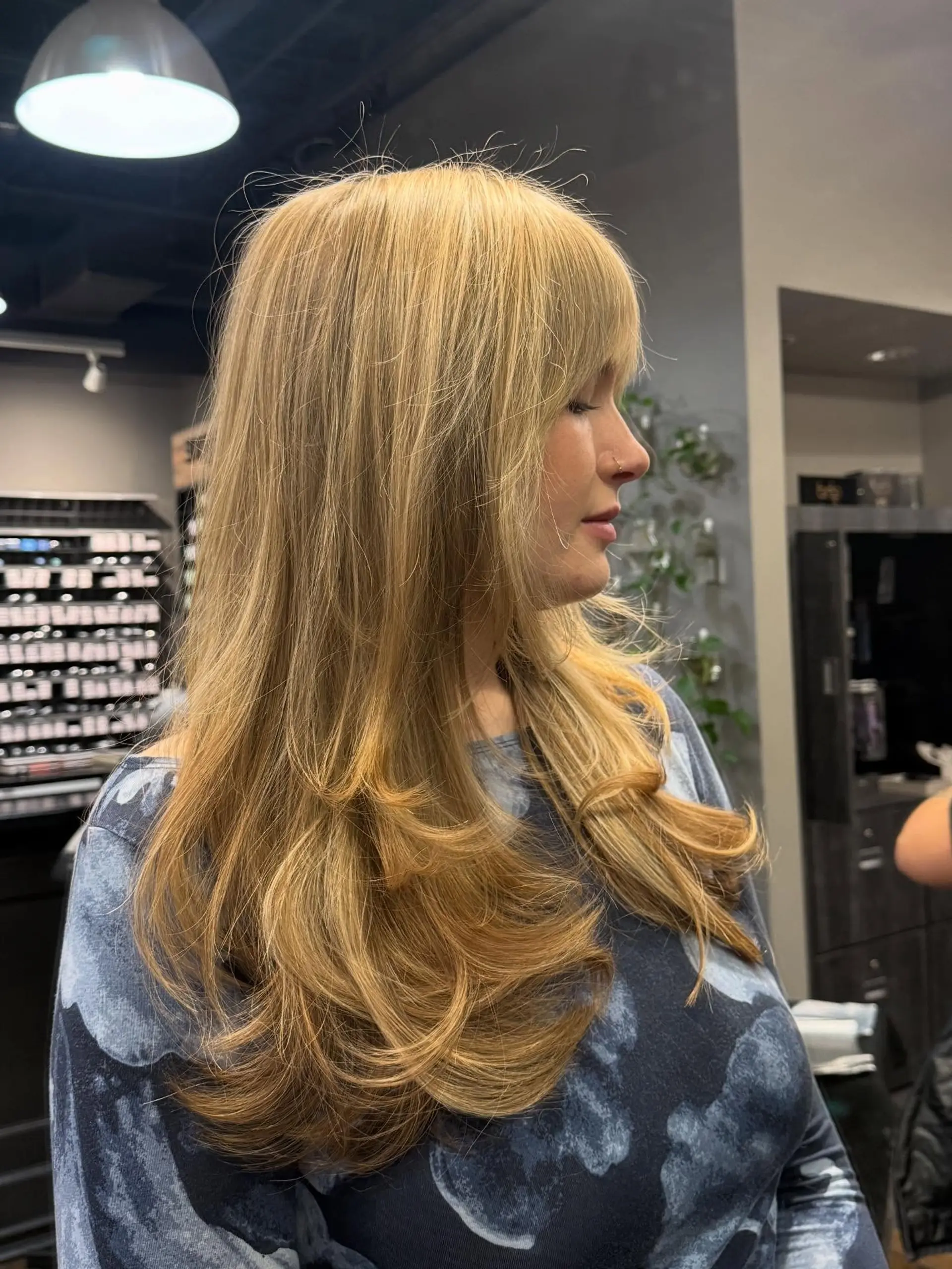 Long warm golden blonde hair styled with sweeping curved layers and a full, textured fringe. 1