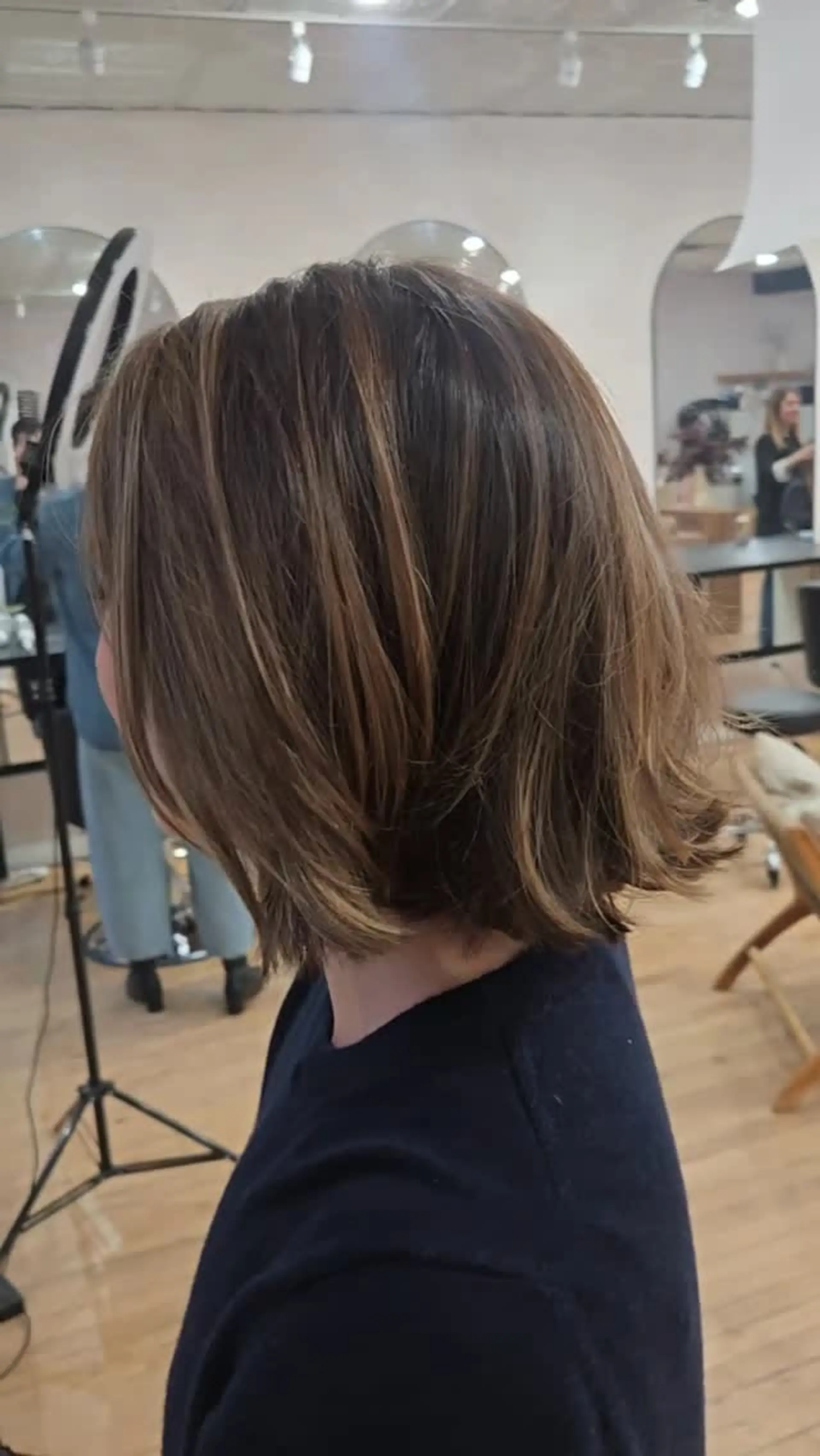 A textured chin-to-neck length bob haircut featuring dimensional brunette tones with subtle warm highlights. 1