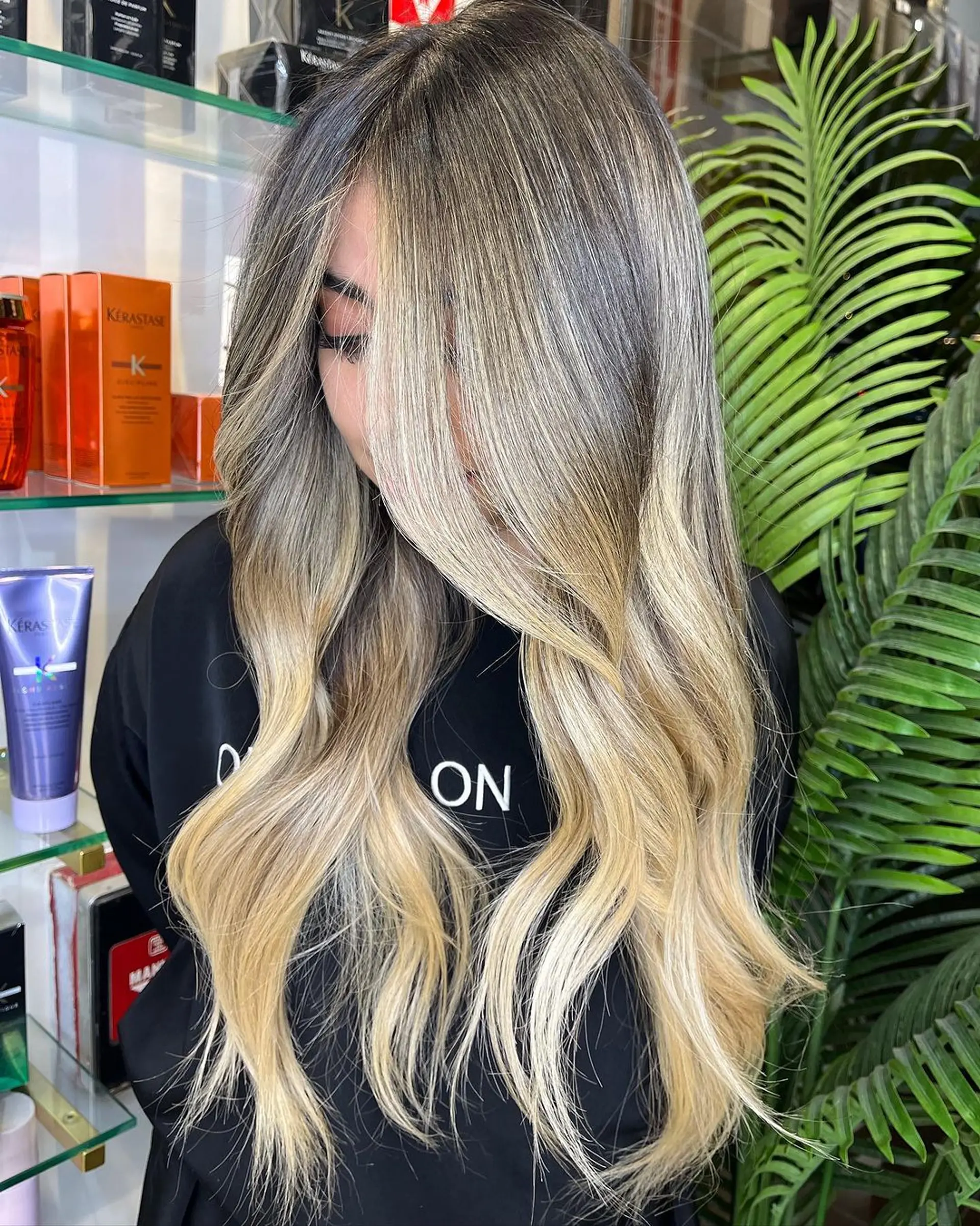 The hairstyle features long, wavy hair crafted with a dark blonde base and gradual platinum and ash blonde balayage highlights, styled in soft beach waves. 2