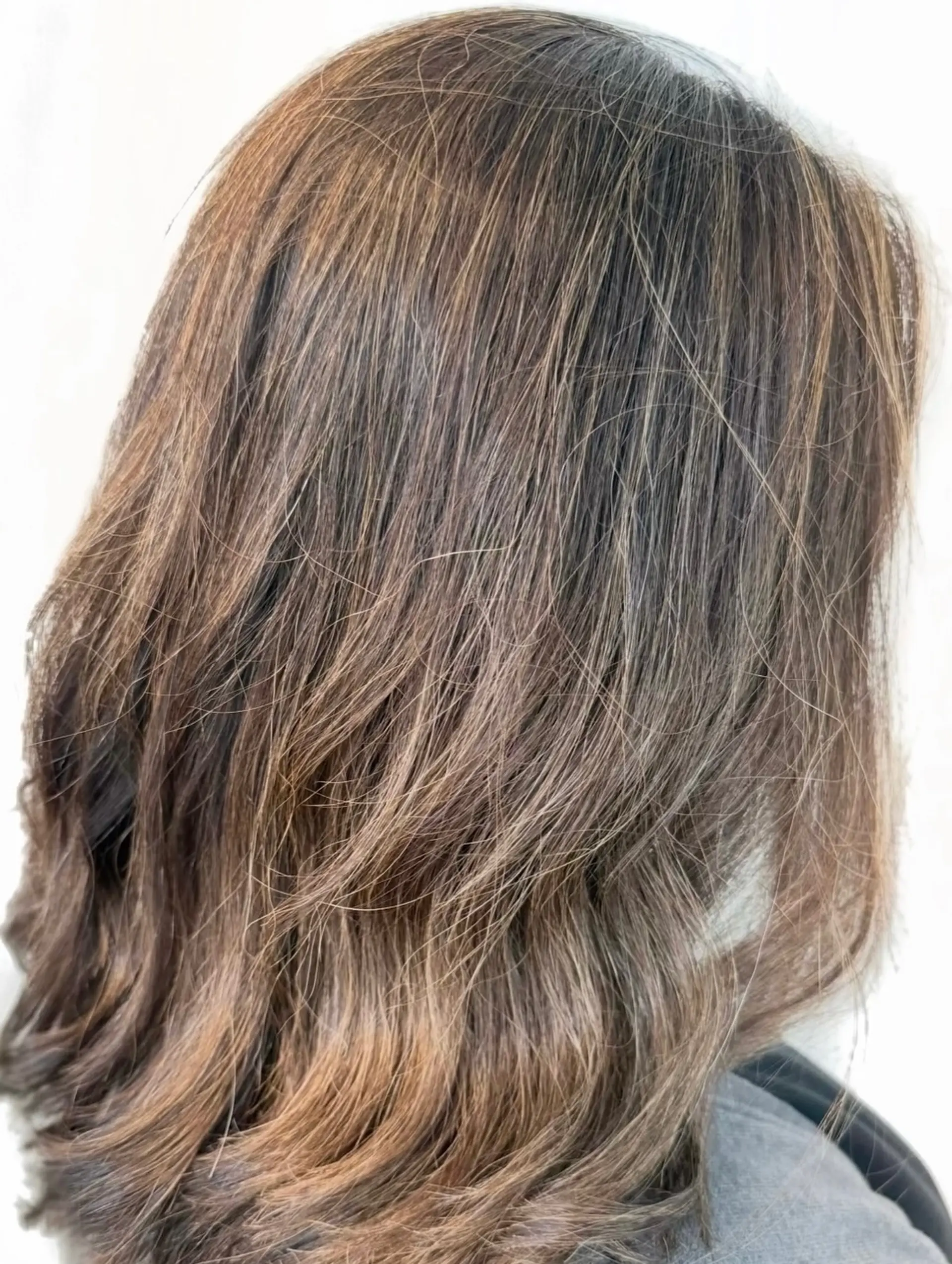 Medium-length wavy brunette hair featuring fine babylights blended seamlessly with natural gray strands and a soft root color. 1
