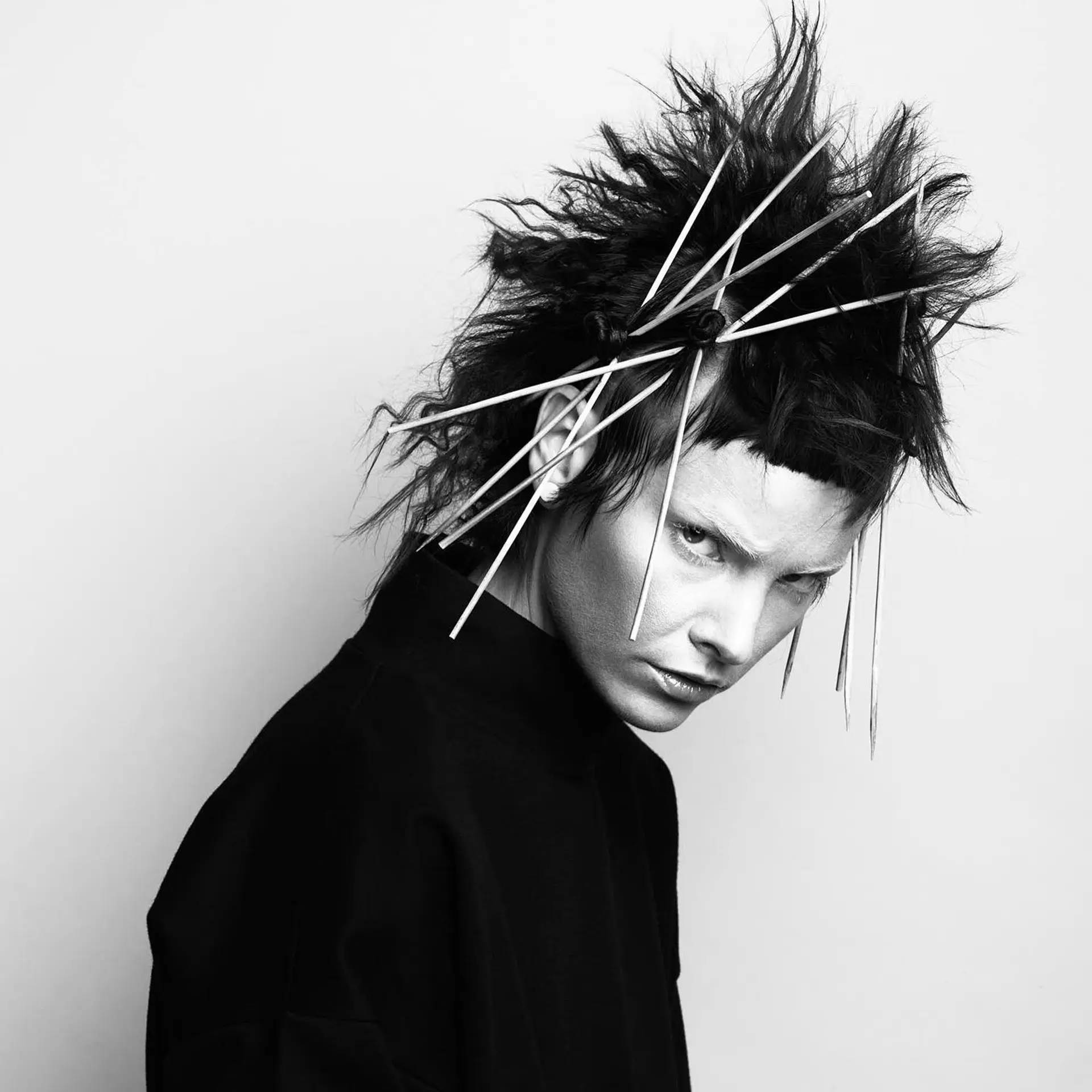 An avant-garde editorial look featuring heavily textured, spiky dark hair with blunt micro bangs and integrated sculptural quill accents. 1