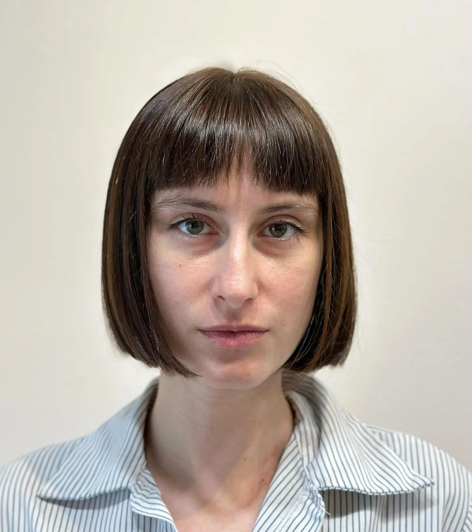 A sleek, short bob with blunt bangs and a symmetrical shape, characterized by sharp edges and a glossy brown finish. 1