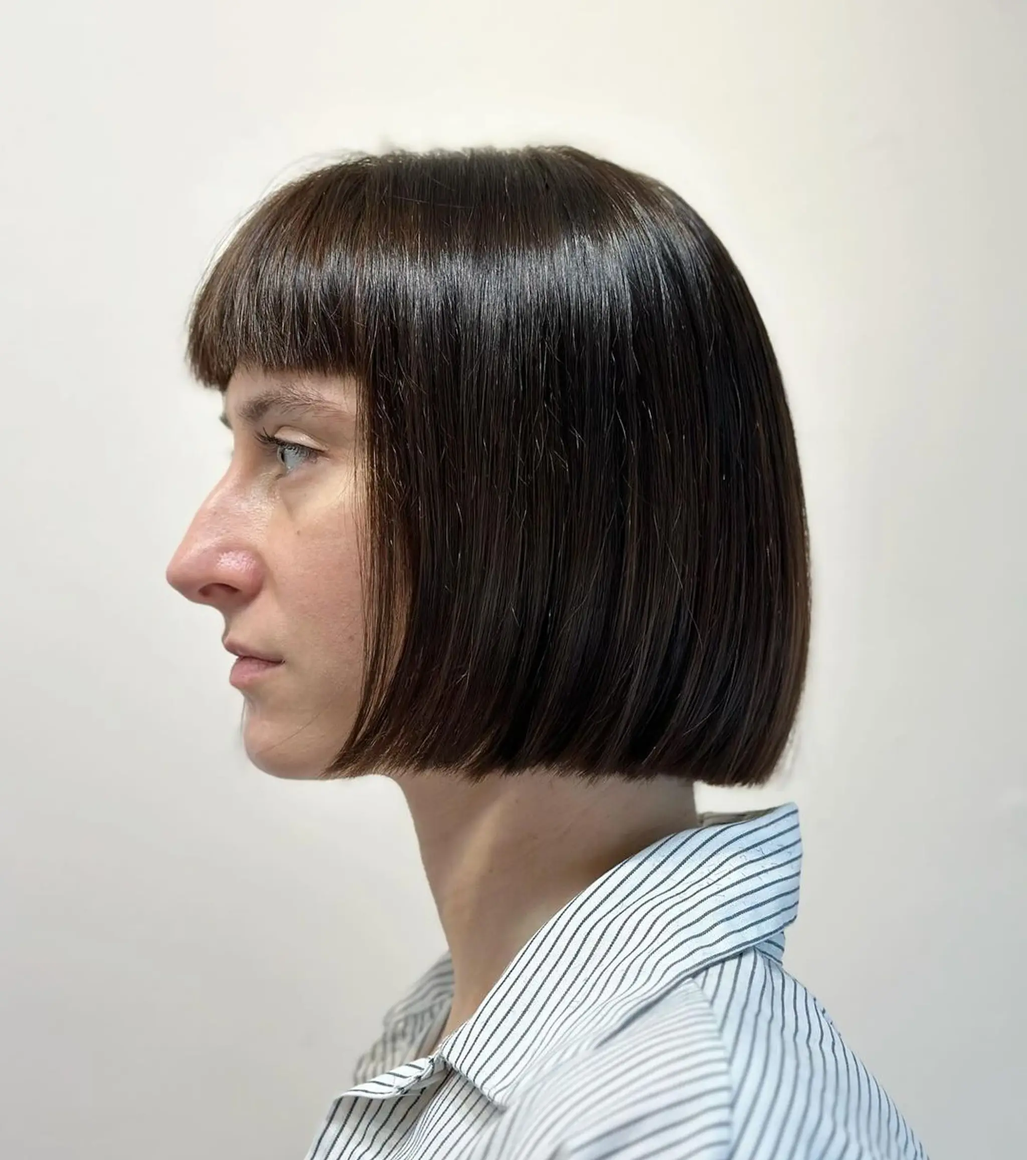 A sleek, short bob with blunt bangs and a symmetrical shape, characterized by sharp edges and a glossy brown finish. 2