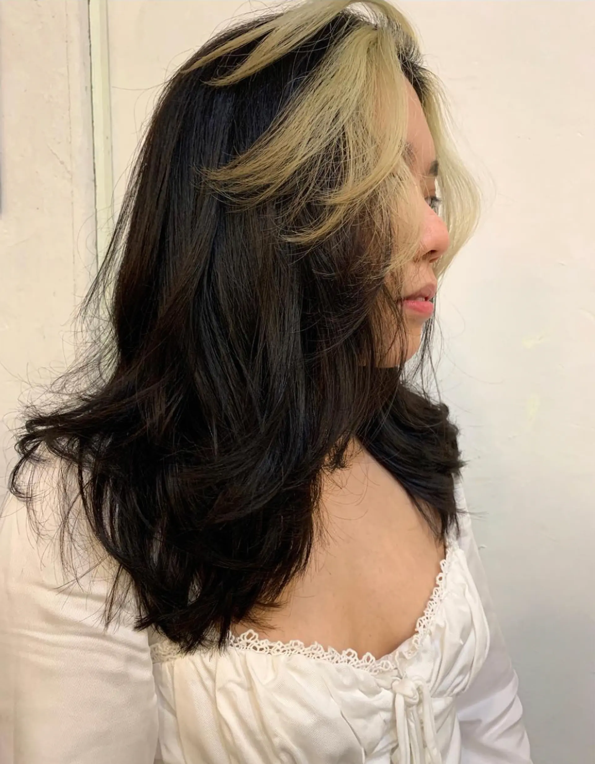 Medium-length black hair with a natural wave and a dramatic face-framing platinum blonde highlight starting from the roots, creating a contrasting halo effect. The wavy texture and layered cut add volume and movement by Emma. 1