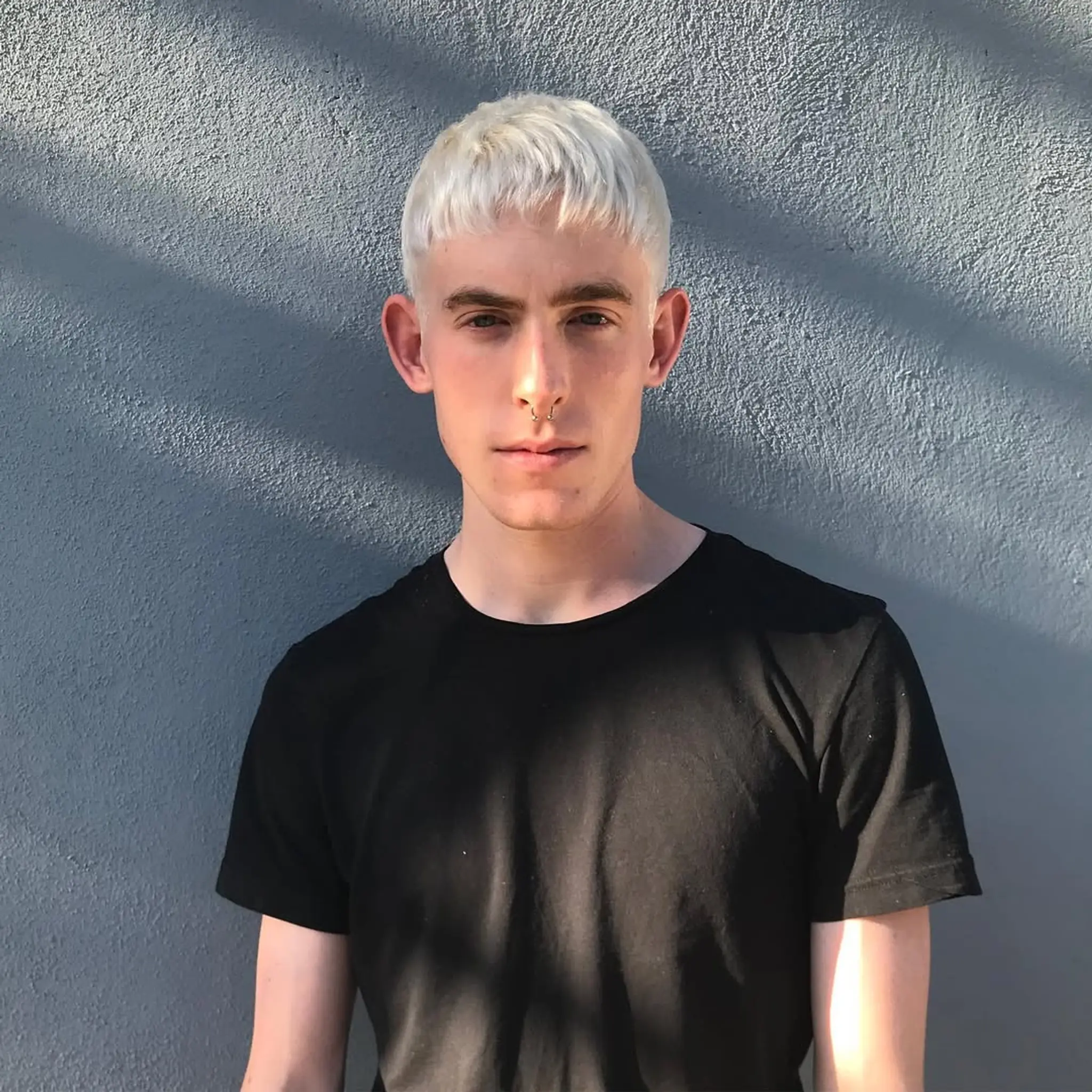 This is a short, straight hairstyle characterized by a platinum blonde dye and an edgy, textured fringe.