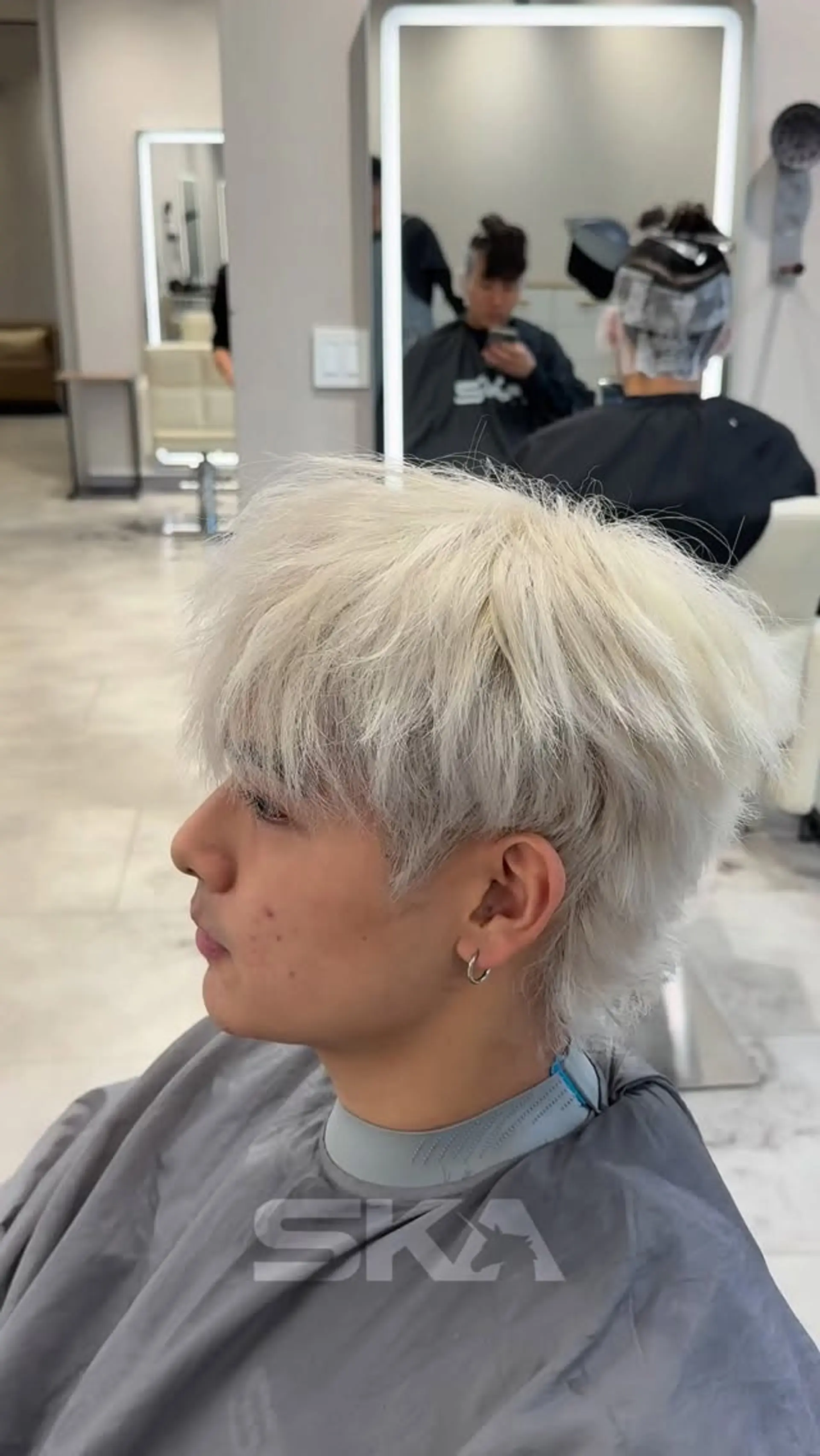 A textured short haircut with forward-swept fringe and a soft tapered neck, colored in an all-over icy platinum blonde. 1