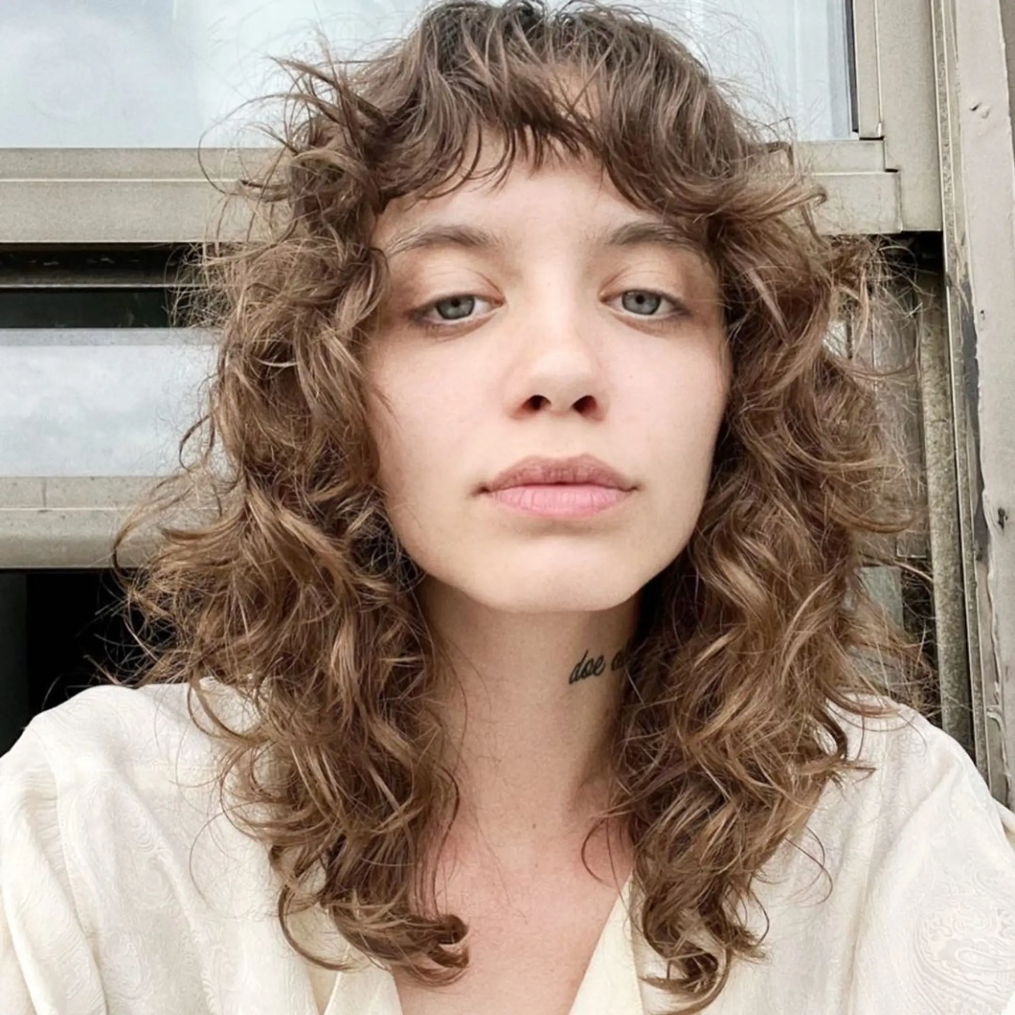A medium-length, curly brown hairstyle with a distinctive shaggy look and natural waves. Features layered curls and a short, uneven fringe for a carefree, bohemian style. haircut by @takeohair