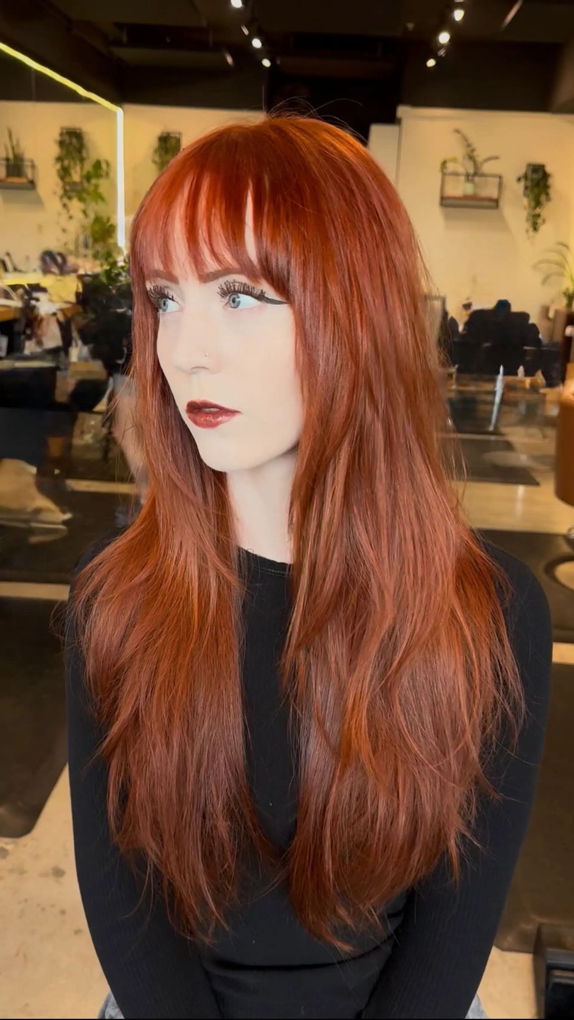 Long vivid copper hair styled straight with face-framing layers and wispy, brow-skimming bangs. 1