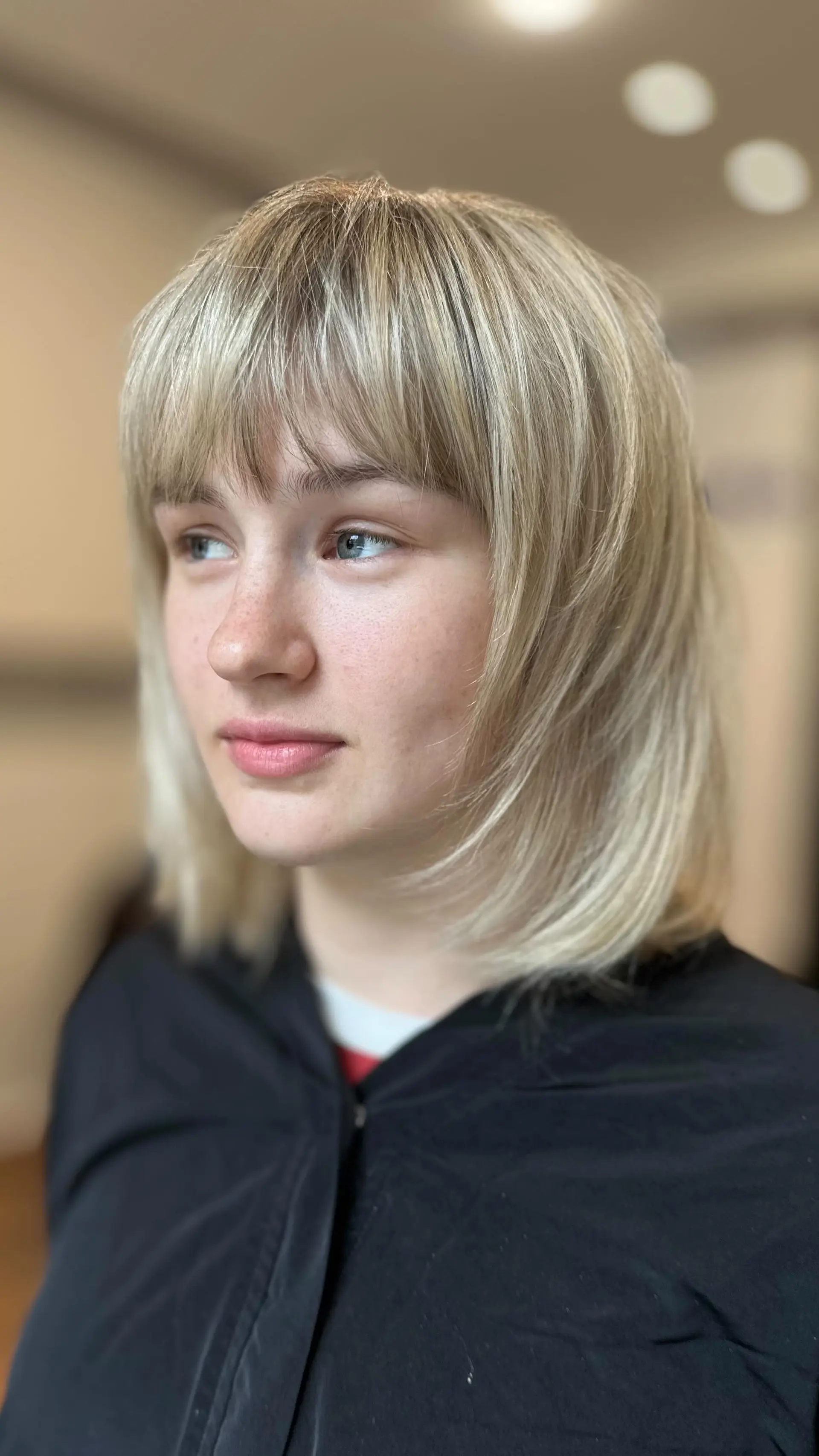 A soft, shoulder-length layered blonde lob featuring full textured bangs and feathered face-framing layers. 1
