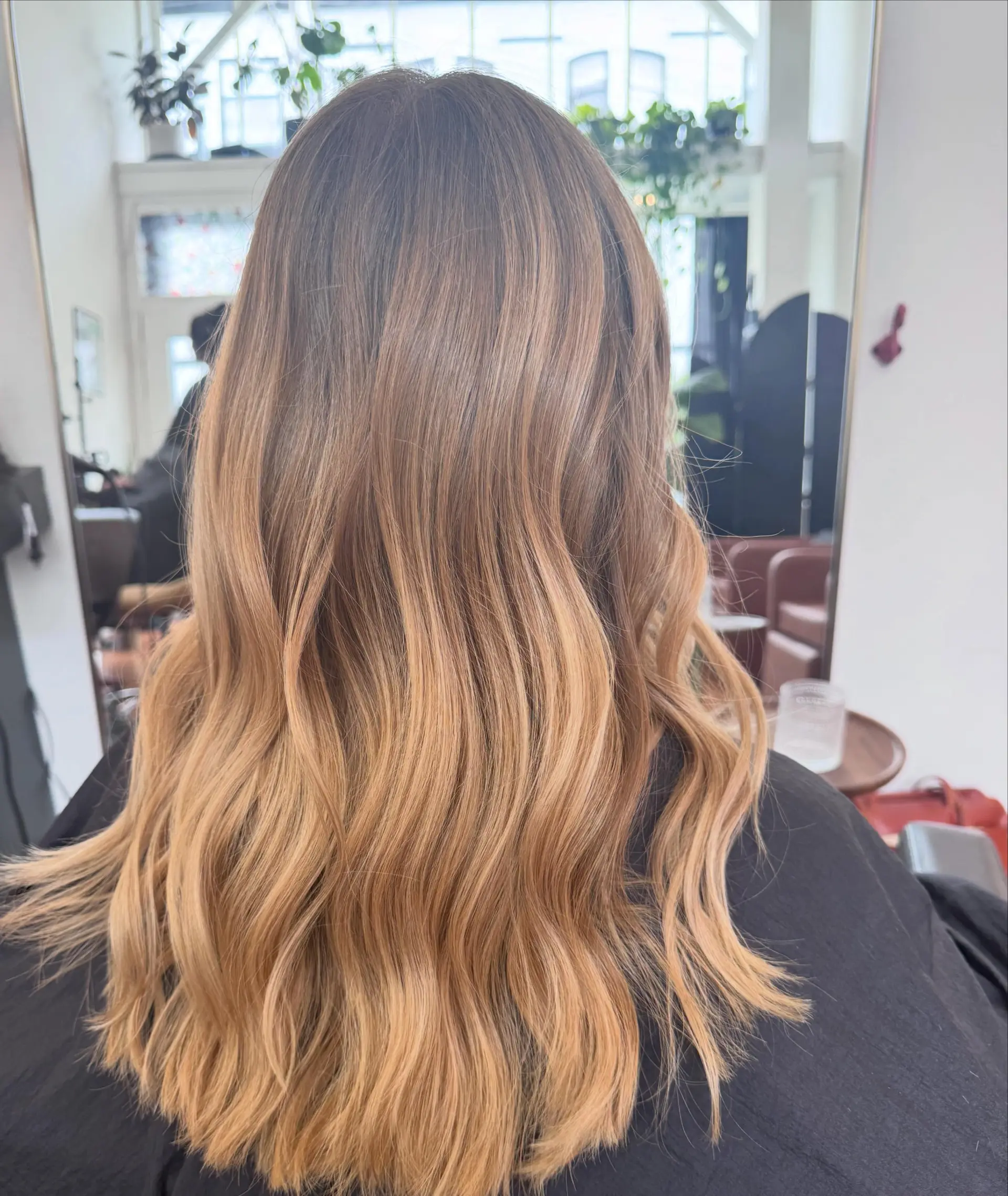 Long hair featuring a seamless warm honey blonde color melt styled in soft, flowing waves. 1