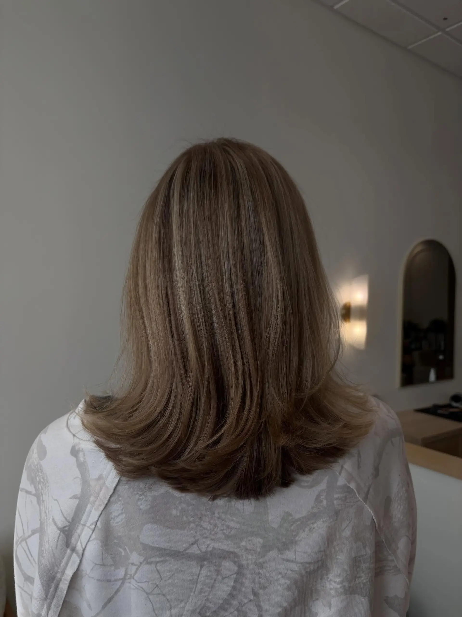 Medium-length soft ash brown hair cut with blended layers and styled with voluminous, outward-flipped ends. 1