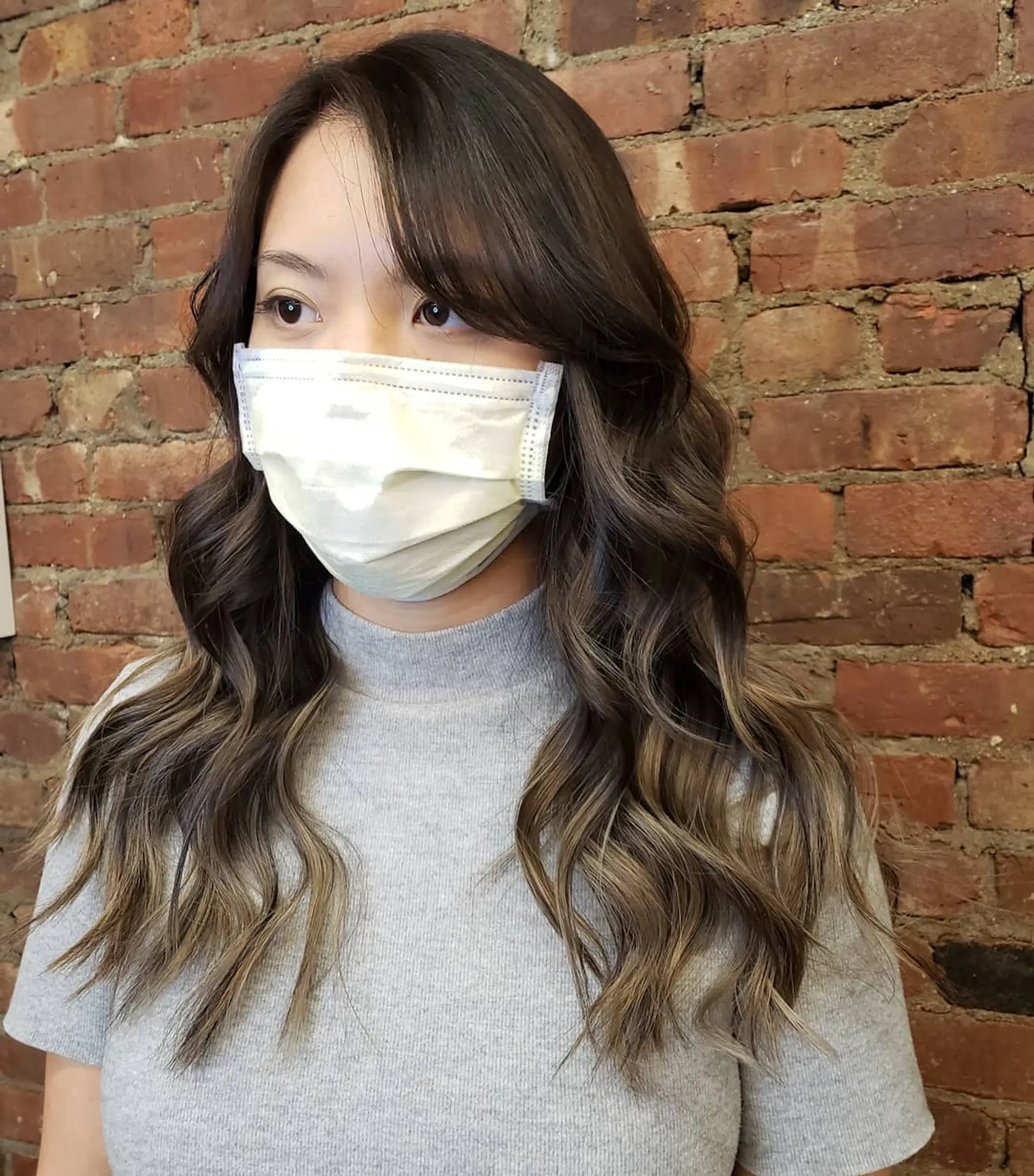 Long brunette hair featuring seamless dimensional balayage highlights styled in soft, loose waves with face-framing side bangs. 1