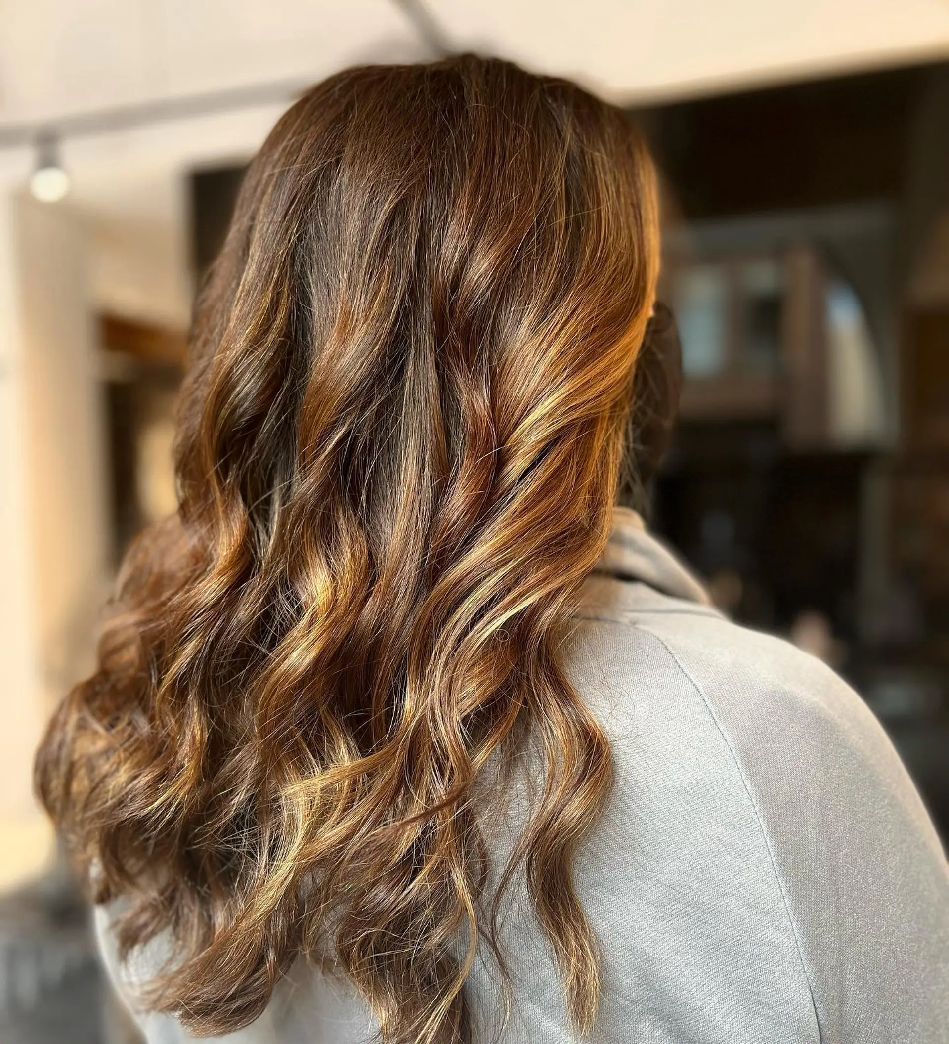 Long dimensional brunette hair styled in loose waves, highlighted with rich caramel and warm honey tones. 1