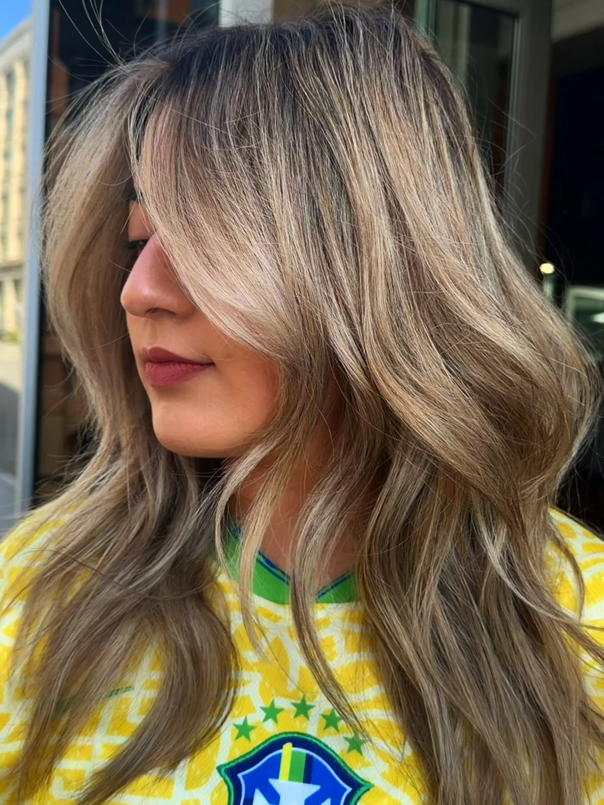 Long beige blonde hair with seamless highlights, styled in soft waves with face-framing curtain bangs. 1