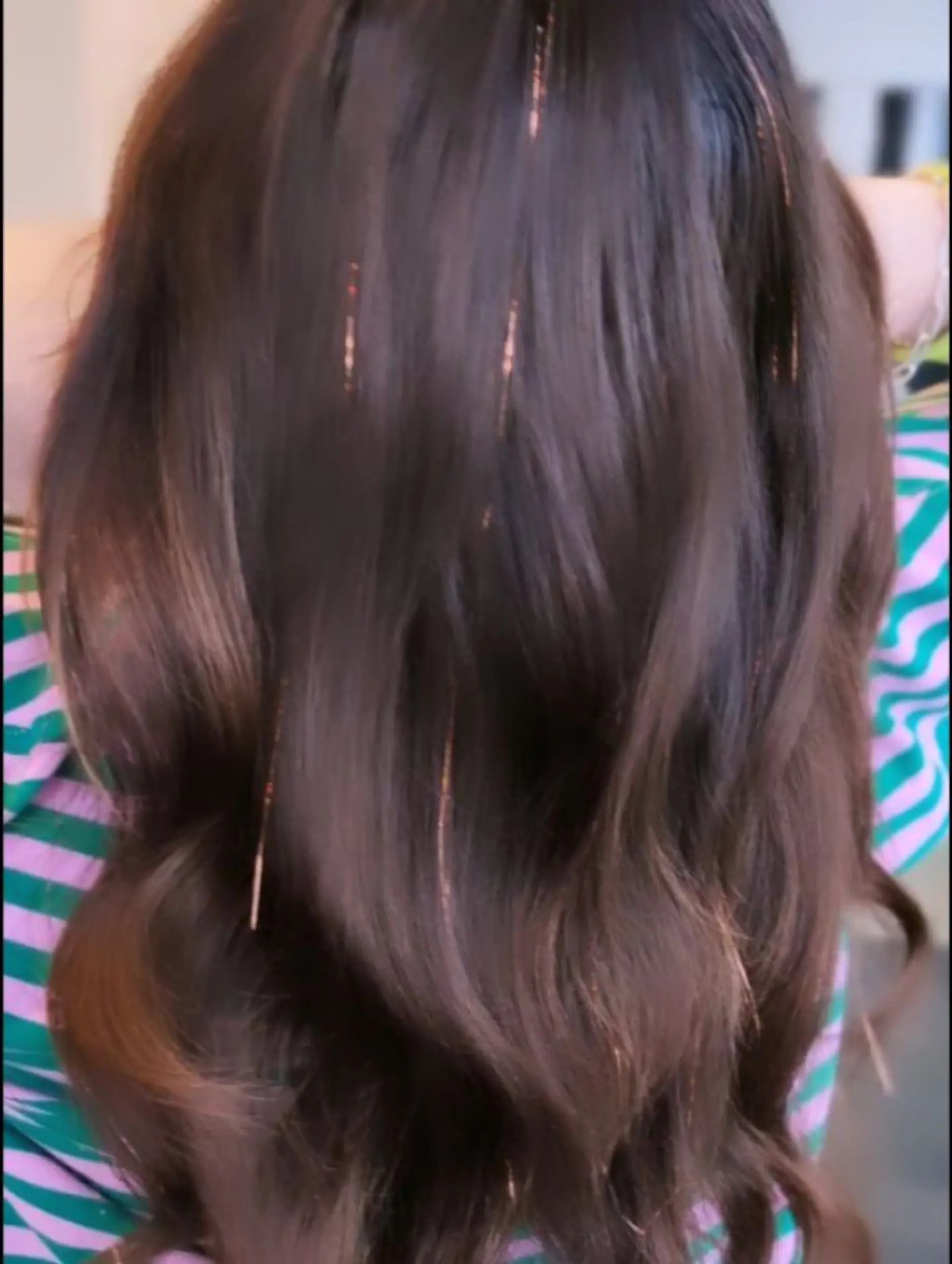 Long dark brown hair styled in soft, loose waves accented with shimmering hair tinsel strands throughout. 1