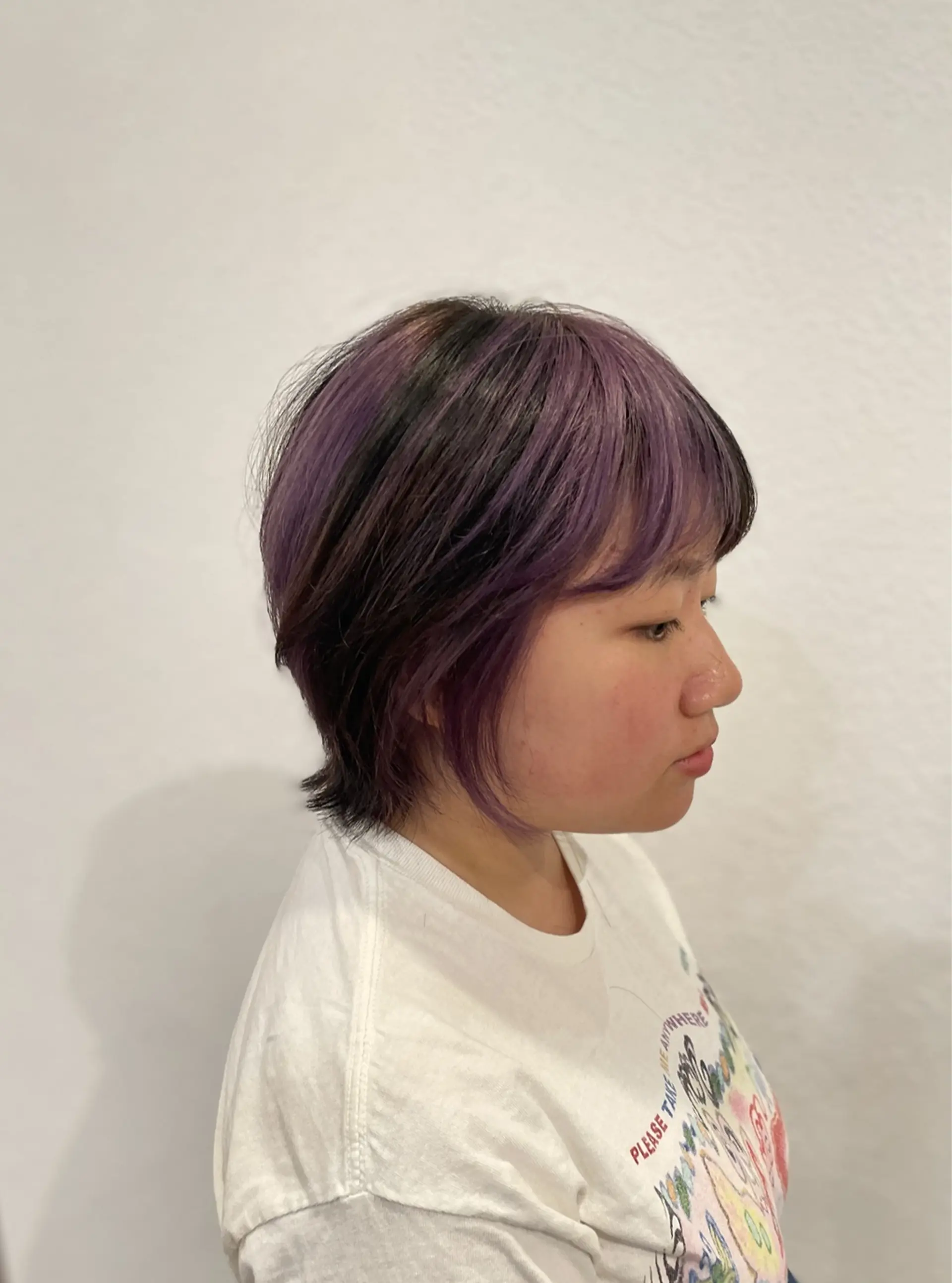 A textured short wolf cut featuring soft face-framing layers, wispy bangs, and vibrant violet balayage highlights over a dark base. 1