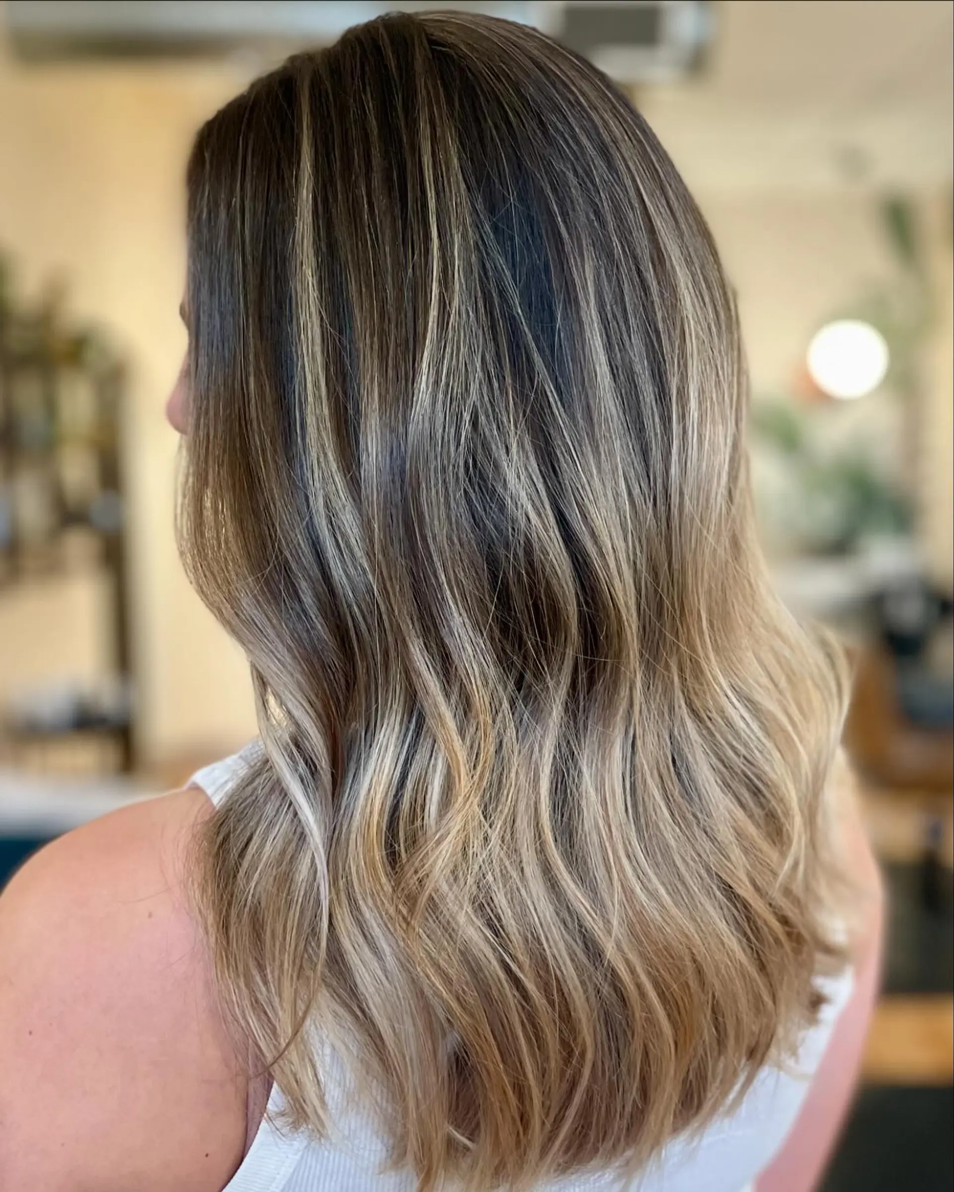 Long layered hair with fine dimensional babylights fading into sun-kissed blonde ends, styled in soft waves. 1