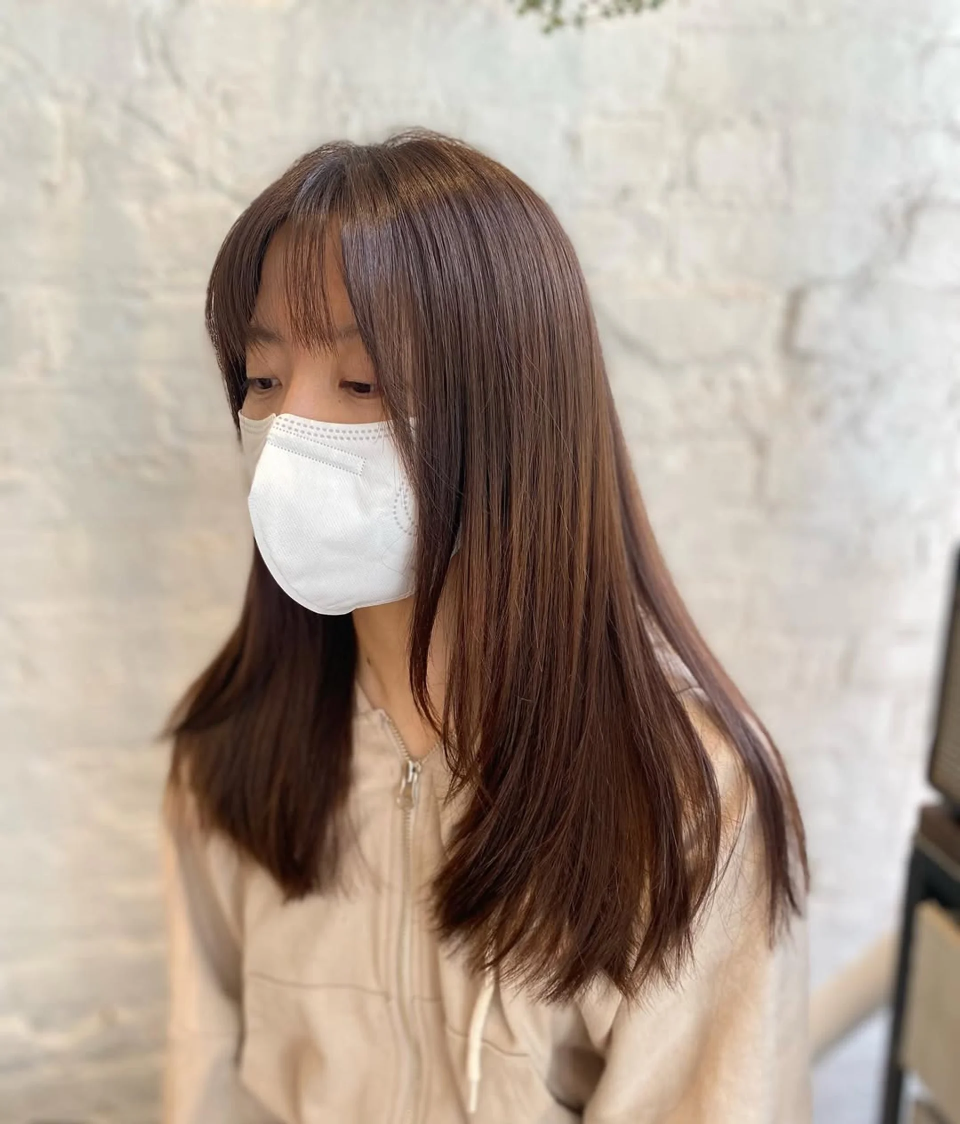 Woman with a medium-length layered haircut featuring curtain bangs and face-framing layers in a bustling NYC salon setting. - Preview 1