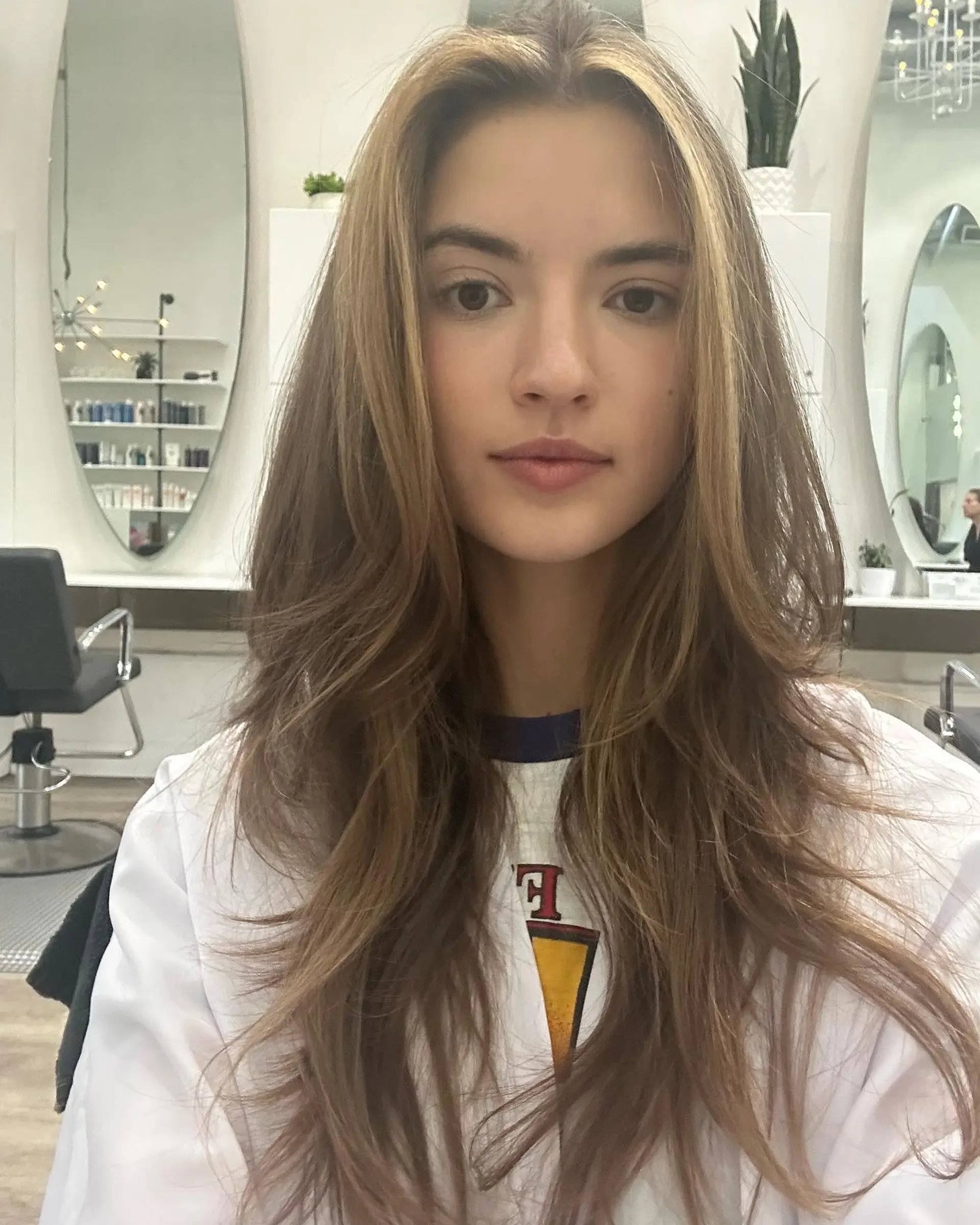 Long layered hair with face-framing curtain bangs and soft feathered ends, accented by subtle golden highlights. 1