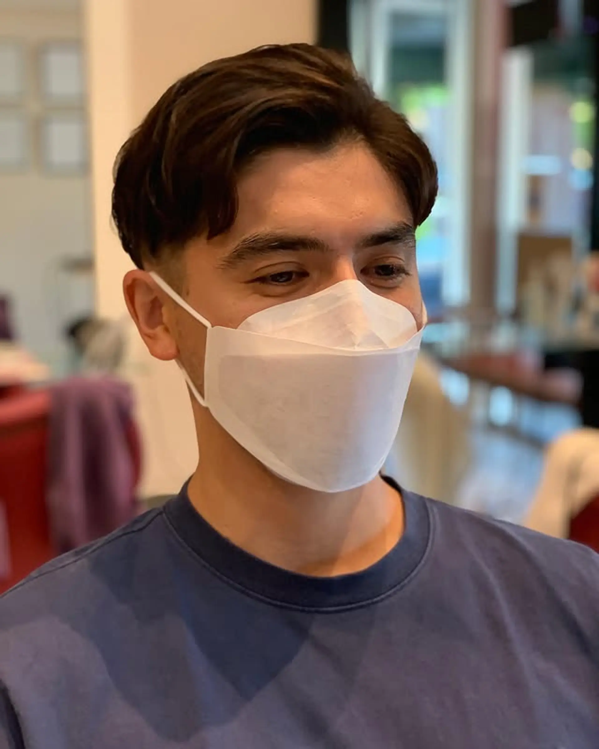 A modern men's haircut with short, tapered sides and a longer, textured top that showcases natural wavy texture, styled by sweeping the hair back and to the side for a relaxed yet polished finish. 1