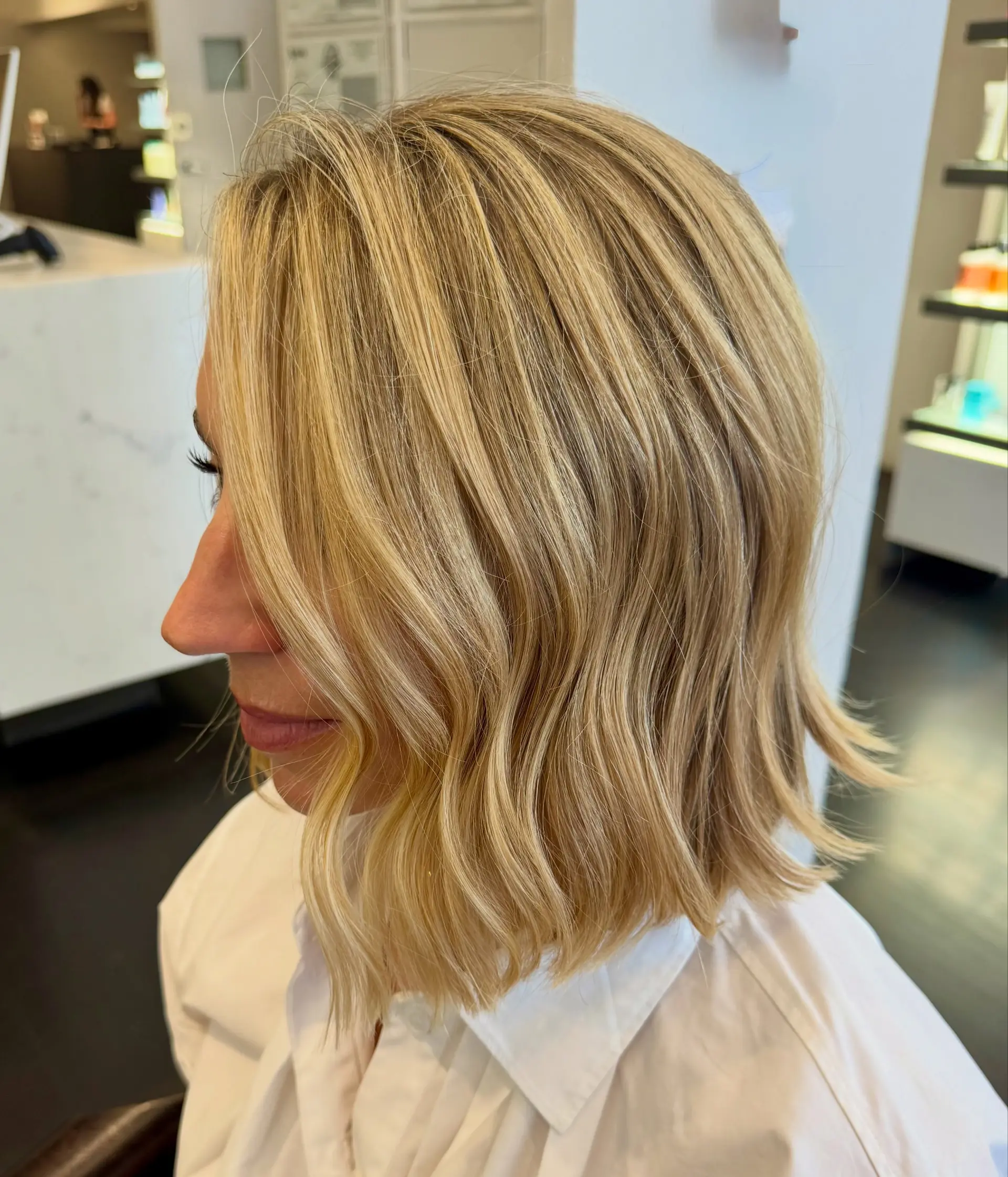 A textured neck-length bob styled with gentle, soft waves in a dimensional buttery blonde. 1