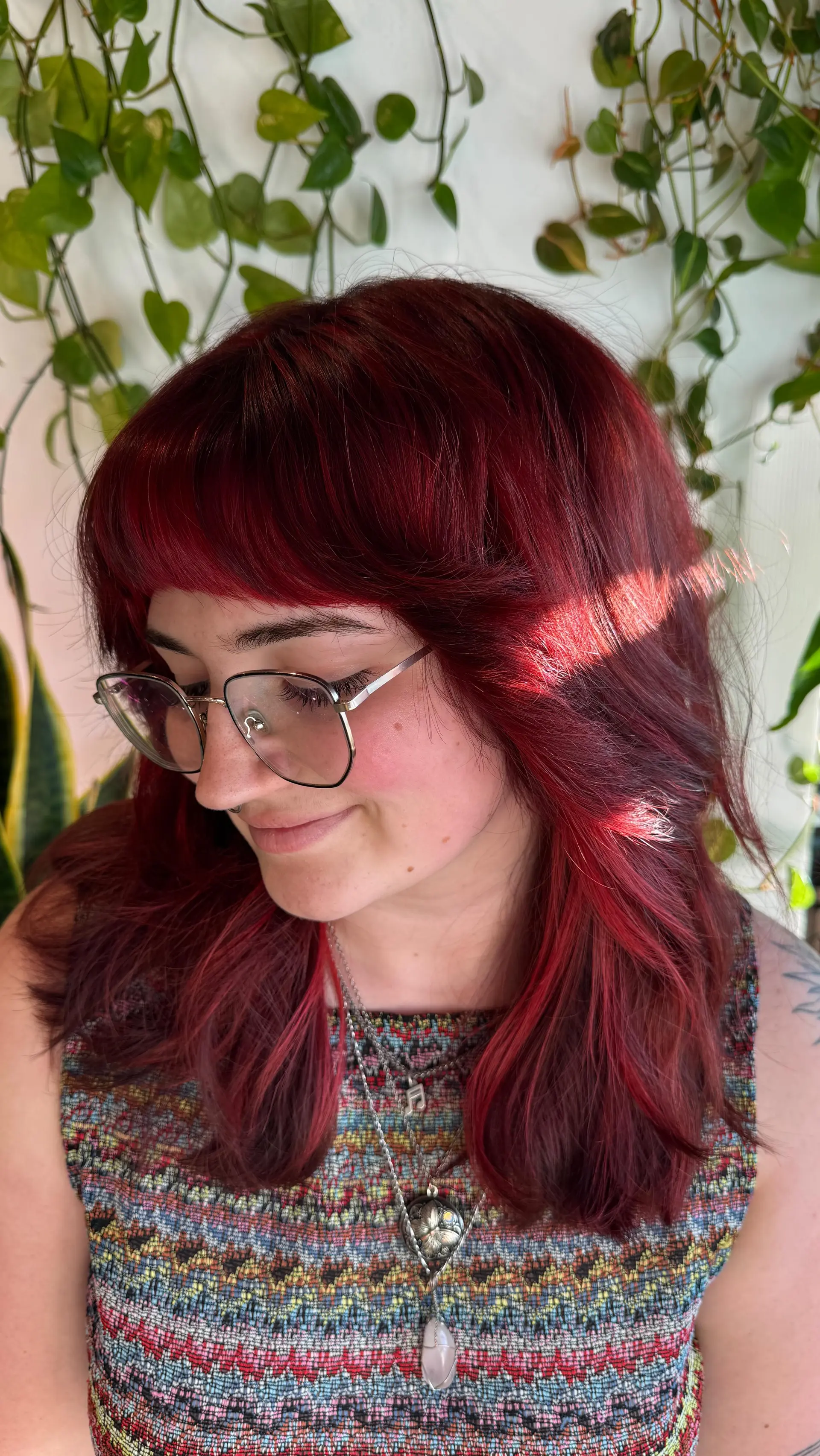 A medium-length layered cut featuring rich crimson red color paired with textured bangs and soft face-framing layers. 1