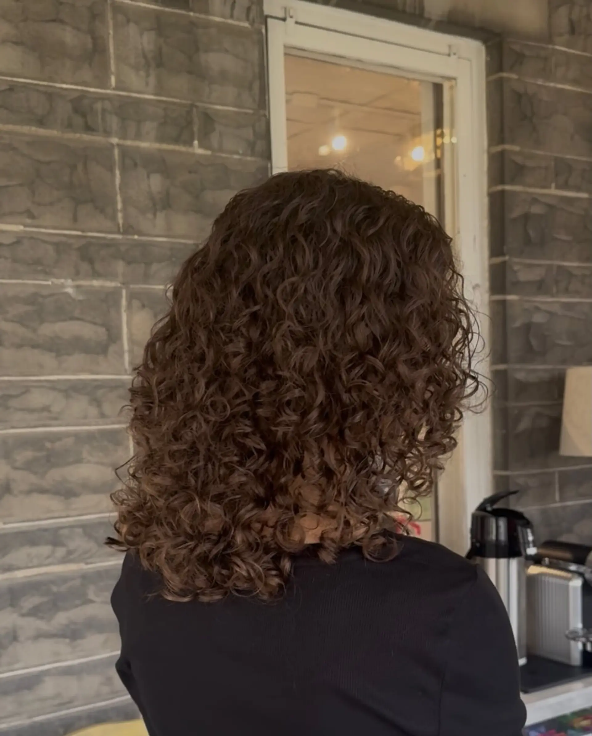 Medium-length layered haircut styled with well-defined, bouncy brunette curls and natural volume. 1